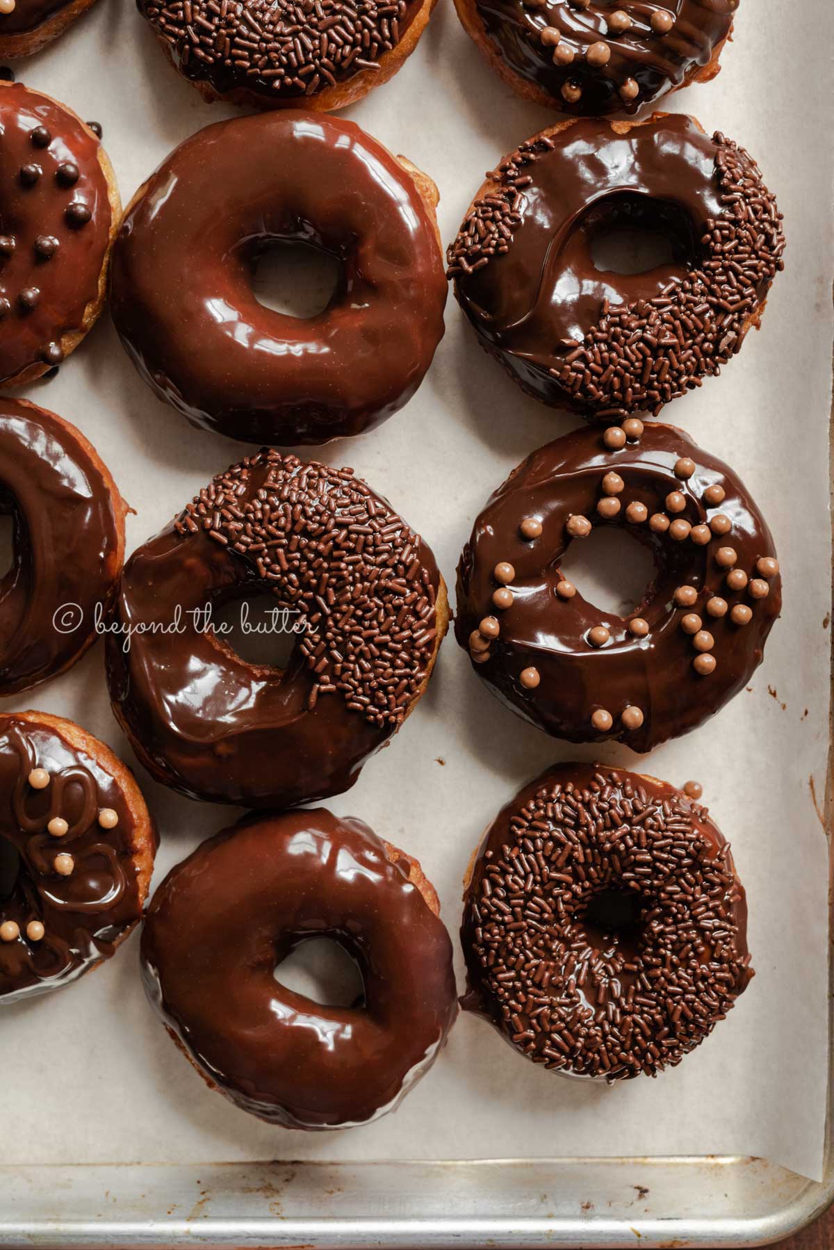 Chocolate glazed decorated donuts on a parchment paper lined baking sheet | All Images © Luyiz™