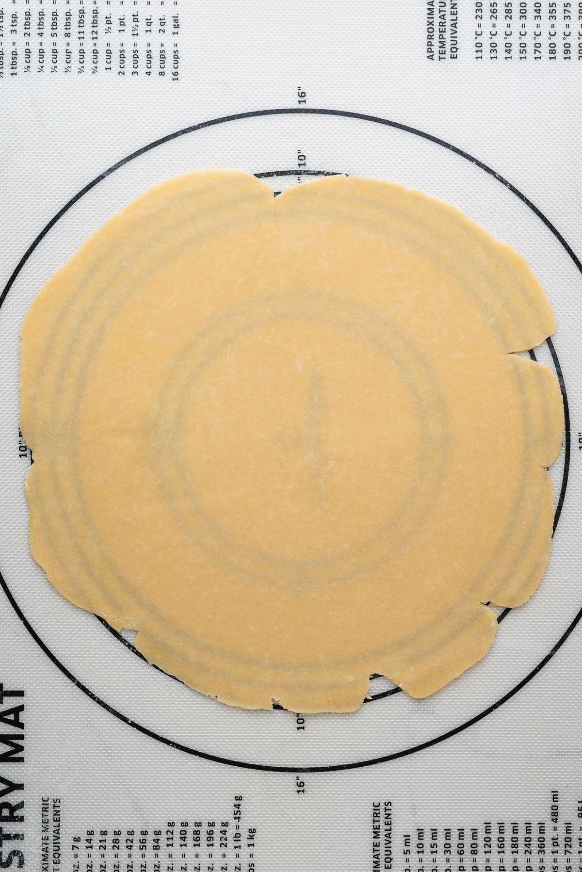 Rolled out pie dough on a white silicone lined pastry mat.