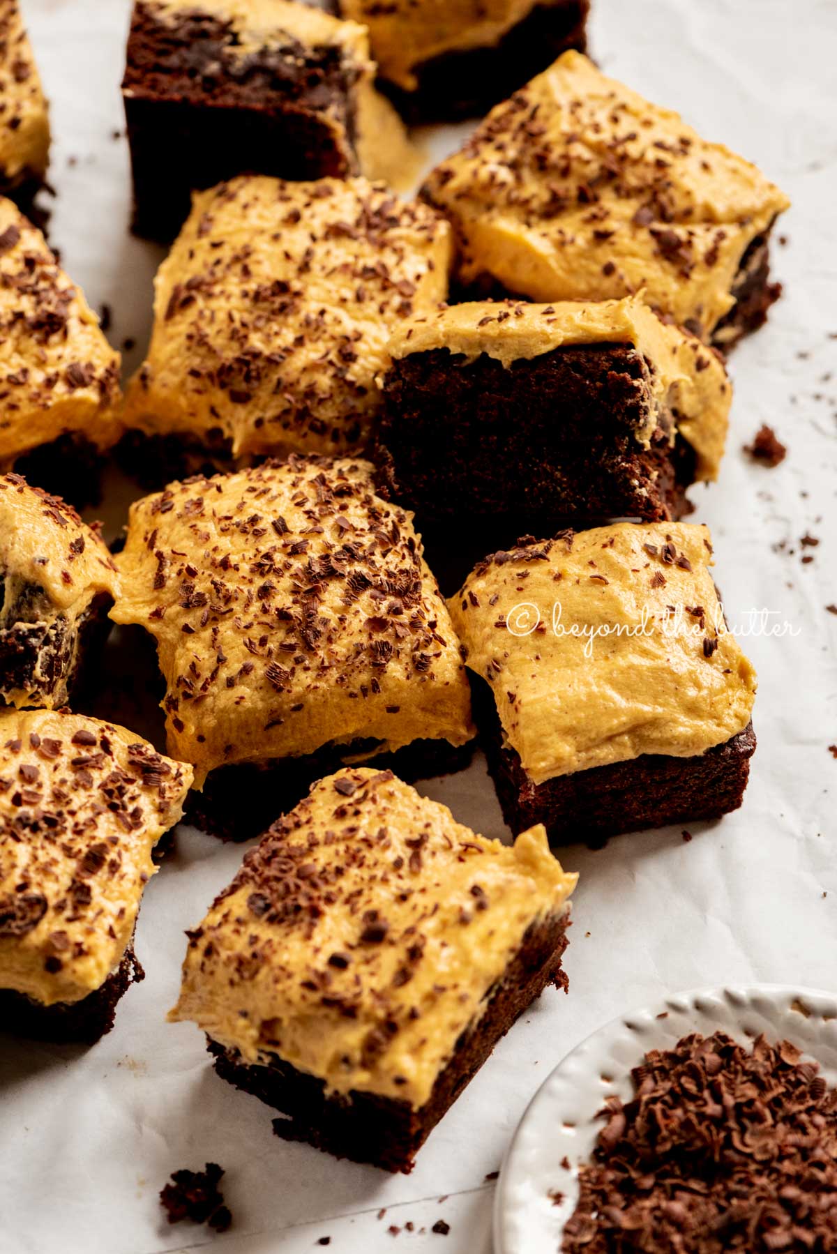 pumpkin frosted brownies randomly placed on parchment paper with a side bowl of chocolate shavings | All Images © Luyiz™