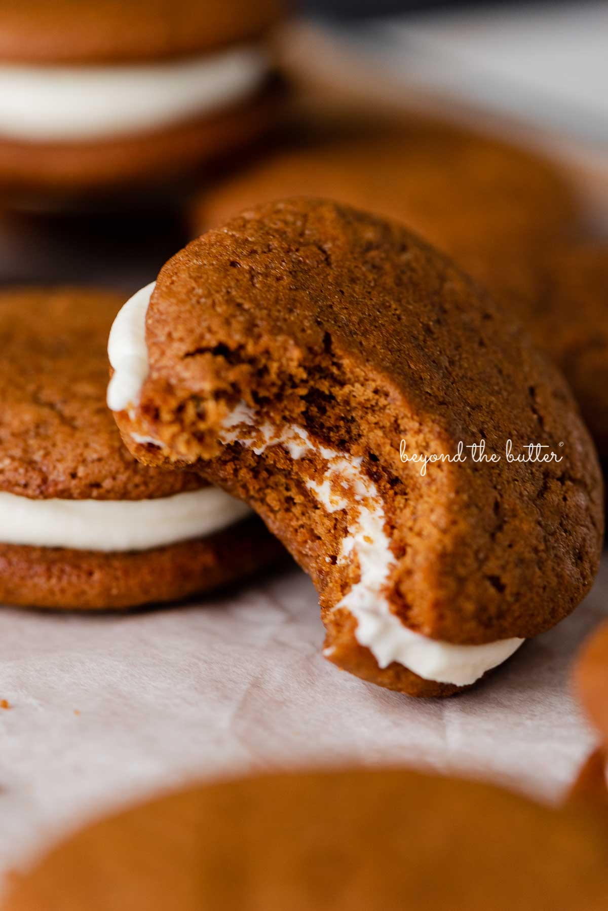 Half eaten homemade gingerbread whoopie pie stacked with more whoopie pies on parchment paper | © Luyiz®
