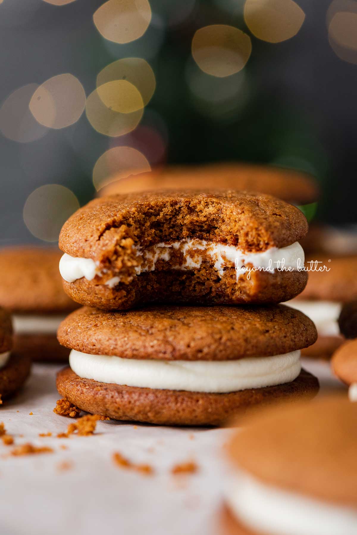 Half eaten gingerbread whoopie pie placed on top of another whoopie pie with a holiday tree background | © Luyiz®