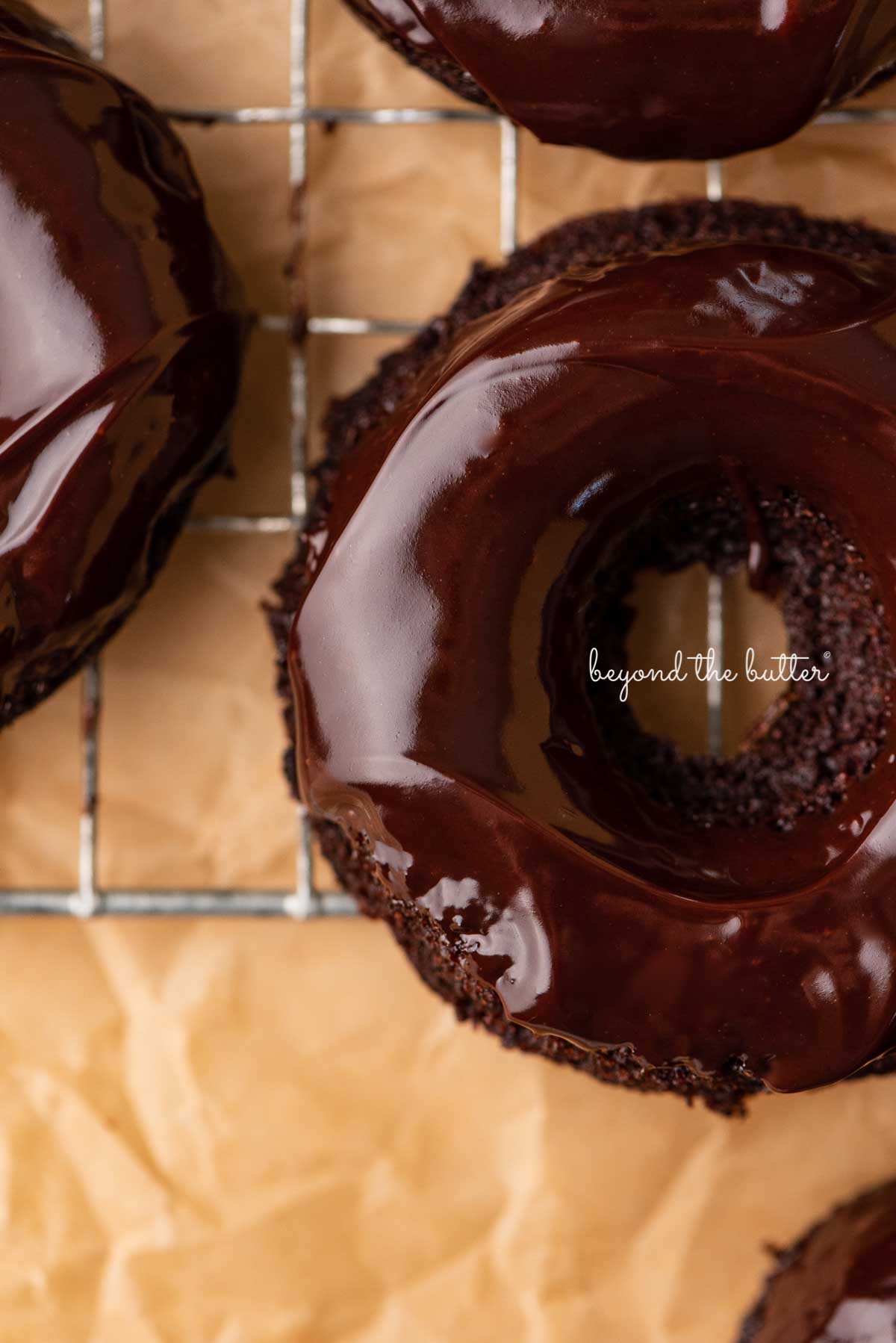 Close up of homemade baked chocolate donuts topped with chocolate ganache on a wire cooling rack | © Luyiz®