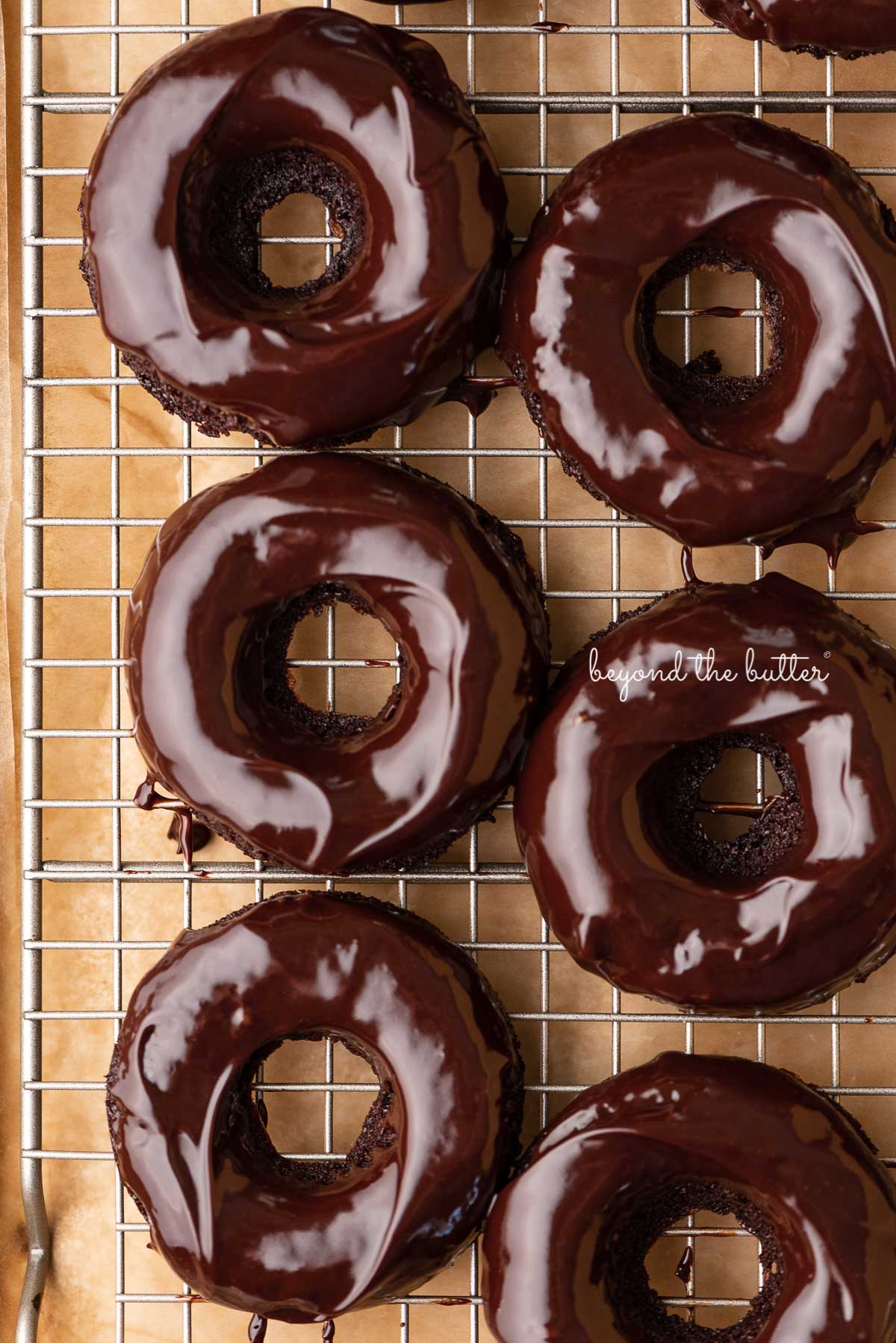 Homemade baked chocolate donuts topped with chocolate ganache on a wire cooling rack | © Luyiz®