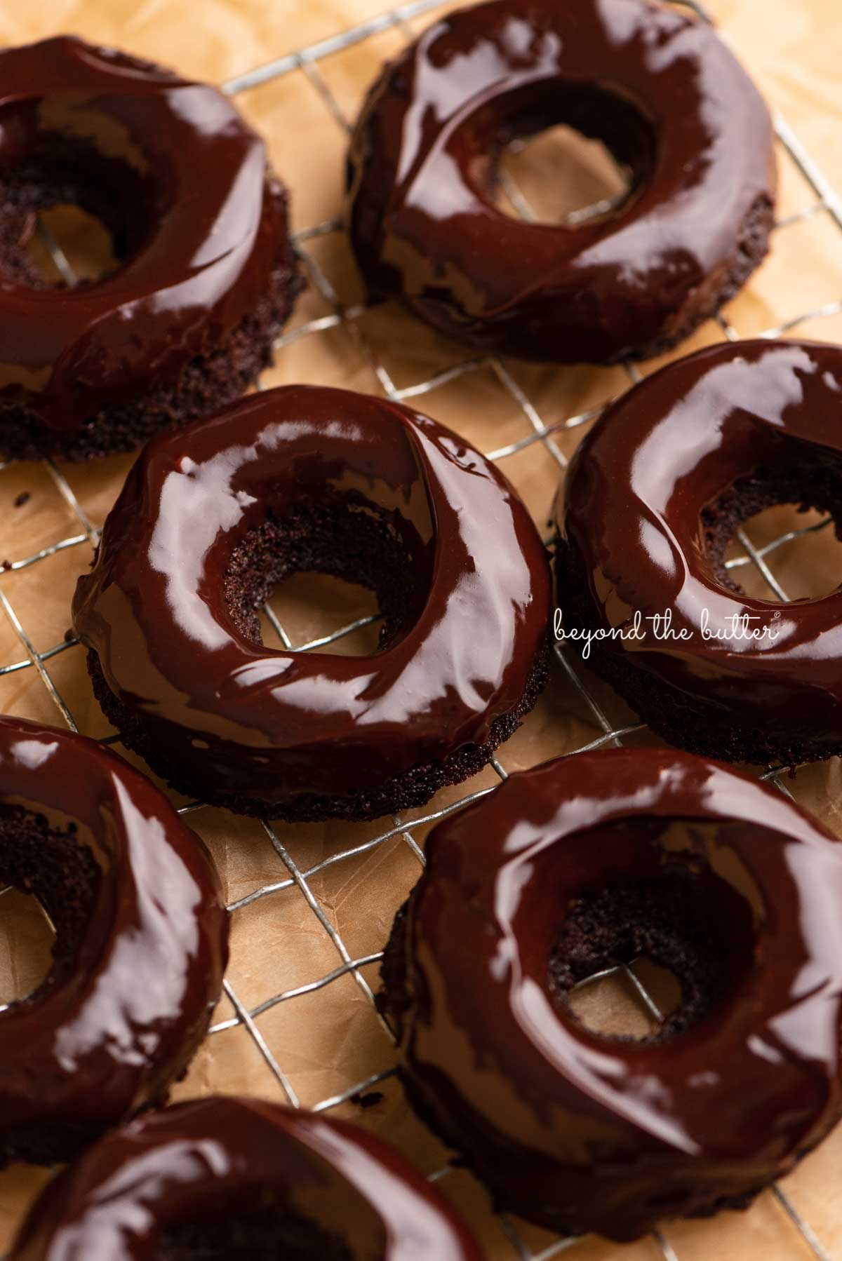 Homemade baked chocolate donuts topped with chocolate ganache on a wire cooling rack | © Luyiz®