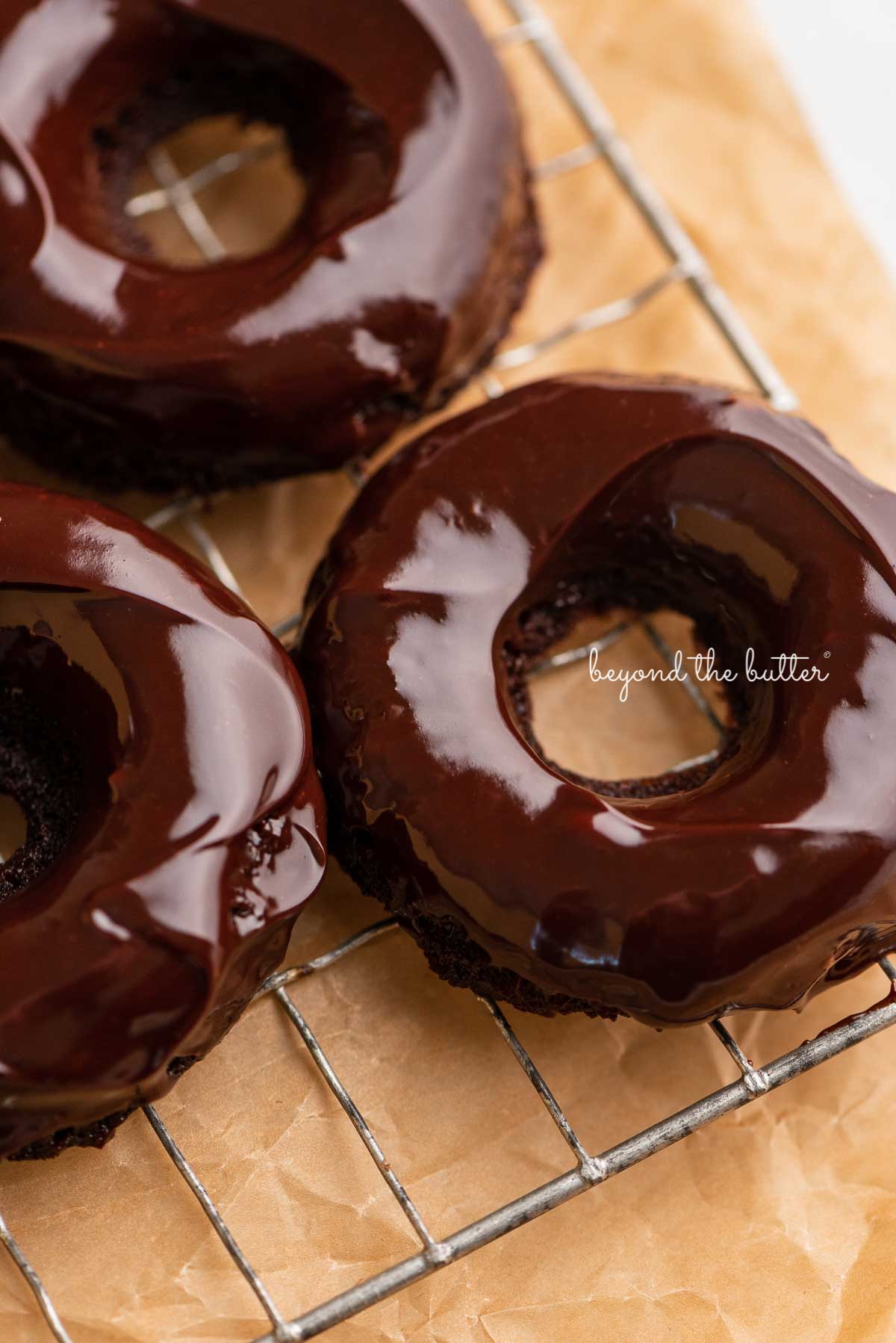 Homemade baked chocolate donuts topped with chocolate ganache on a wire cooling rack | © Luyiz®