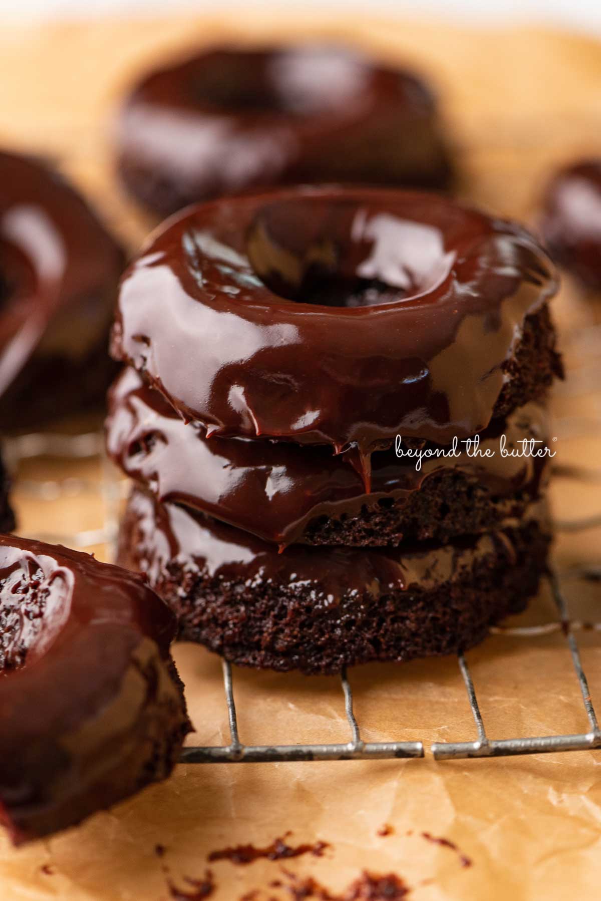 Stacked homemade baked chocolate donuts topped with chocolate ganache on a wire cooling rack | © Luyiz®