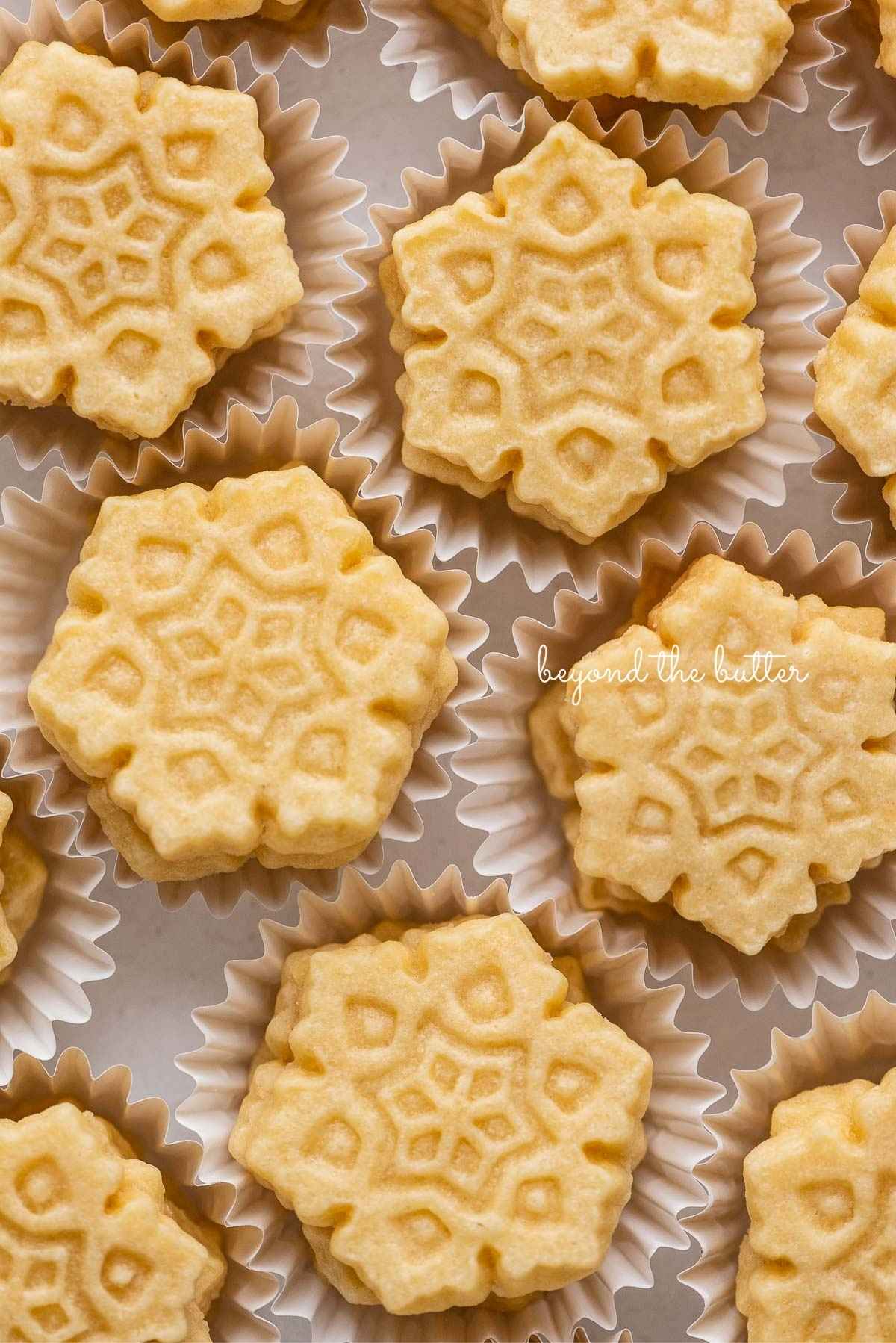 Stacks of homemade butter cookies shaped like snowflakes in white cupcake liners.