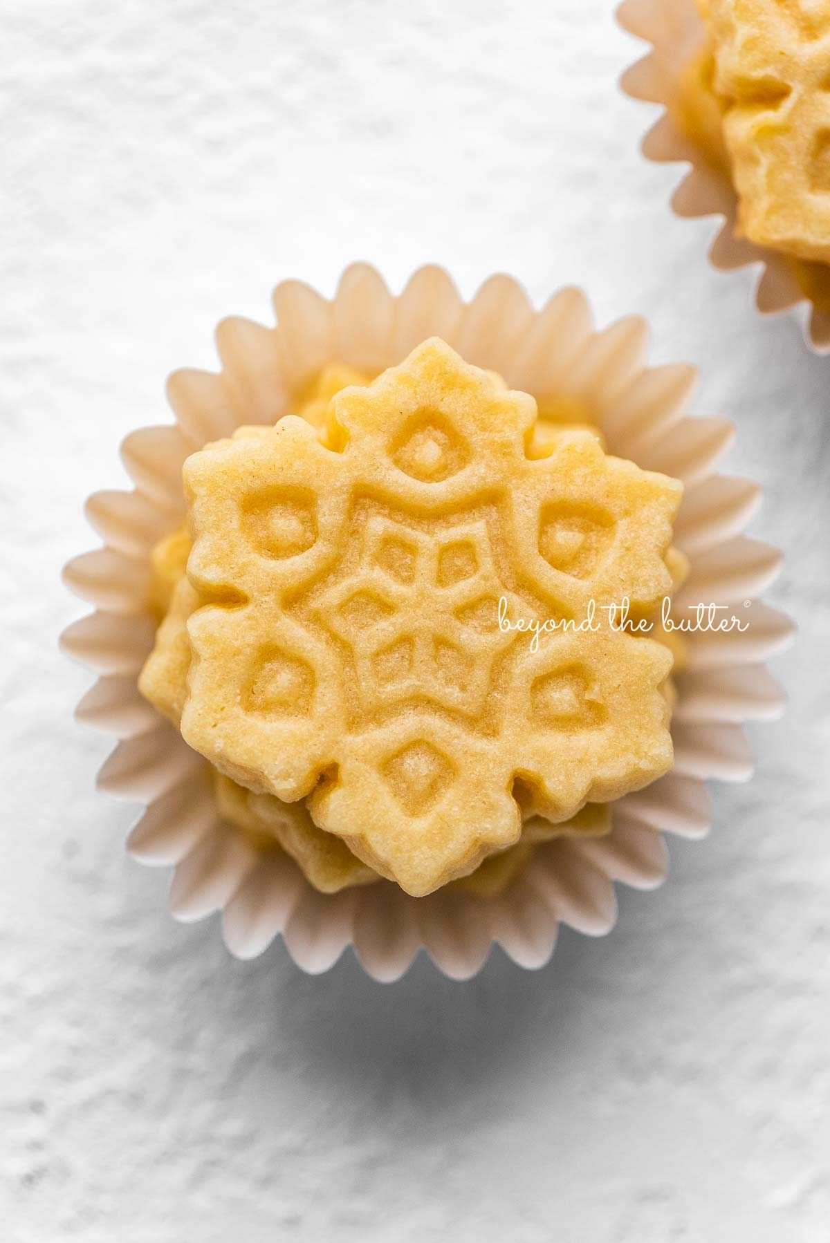 Stacks of butter cookies shaped as snowflakes in mini cupcake liners on a white background.