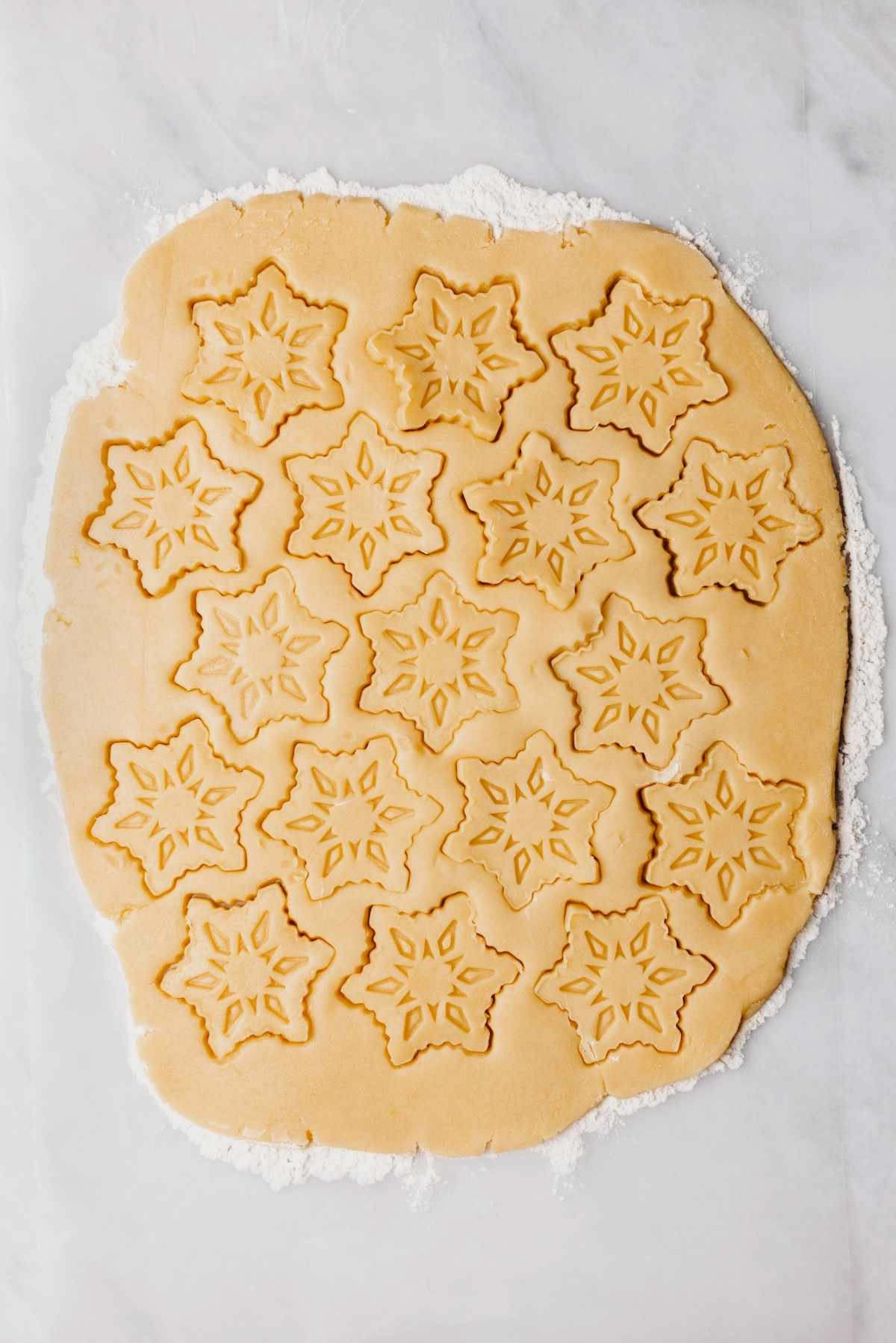 Rolled out homemade butter cookie dough on a lightly floured work surface with snowflake shape stamped into the cookie dough.