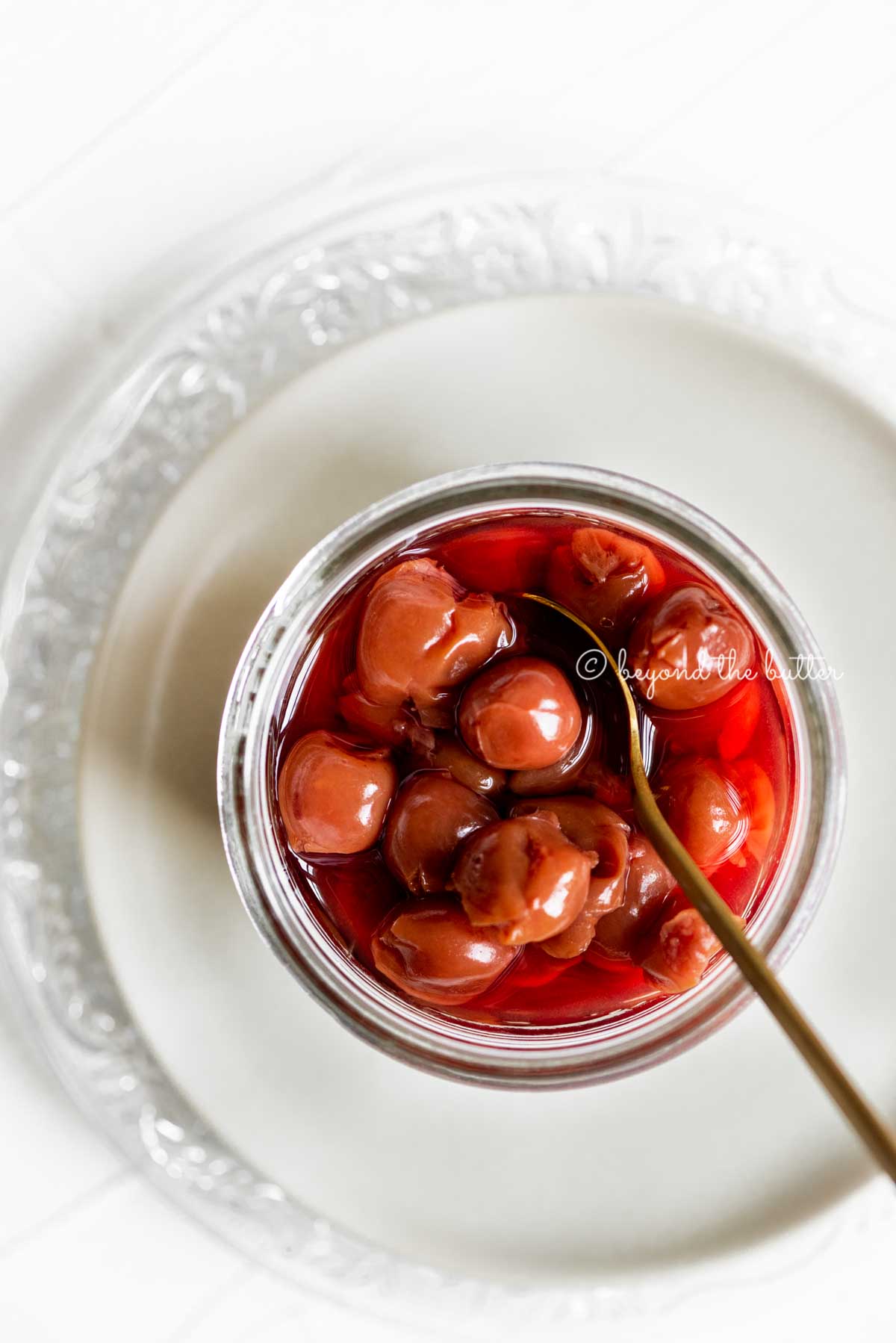Small glass jar of cherries with a spoon on top of 2 plates | All Images © Luyiz™