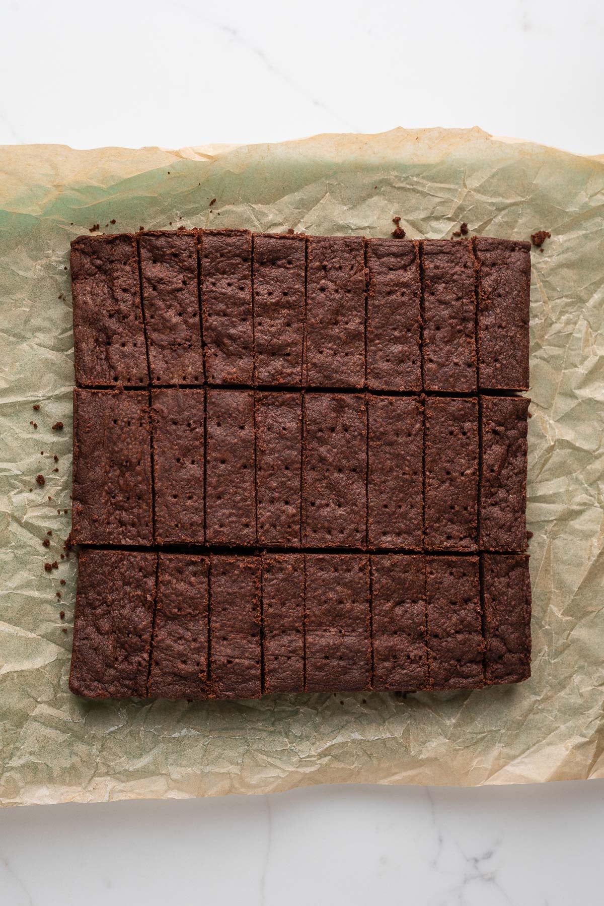 Sliced chocolate shortbread biscuits ted lasso style on a parchment paper lined cutting board and white marbled surface.
