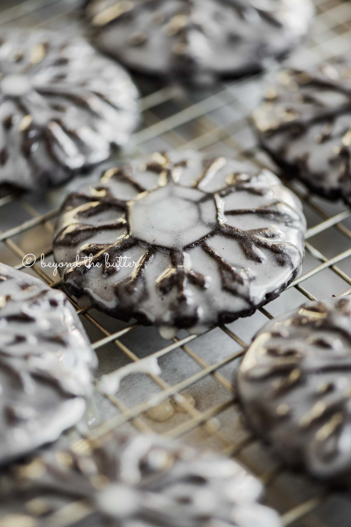 Angled closeup image of homemade oreo snowflake cookies on a wire cooling rack | All Images © Luyiz®