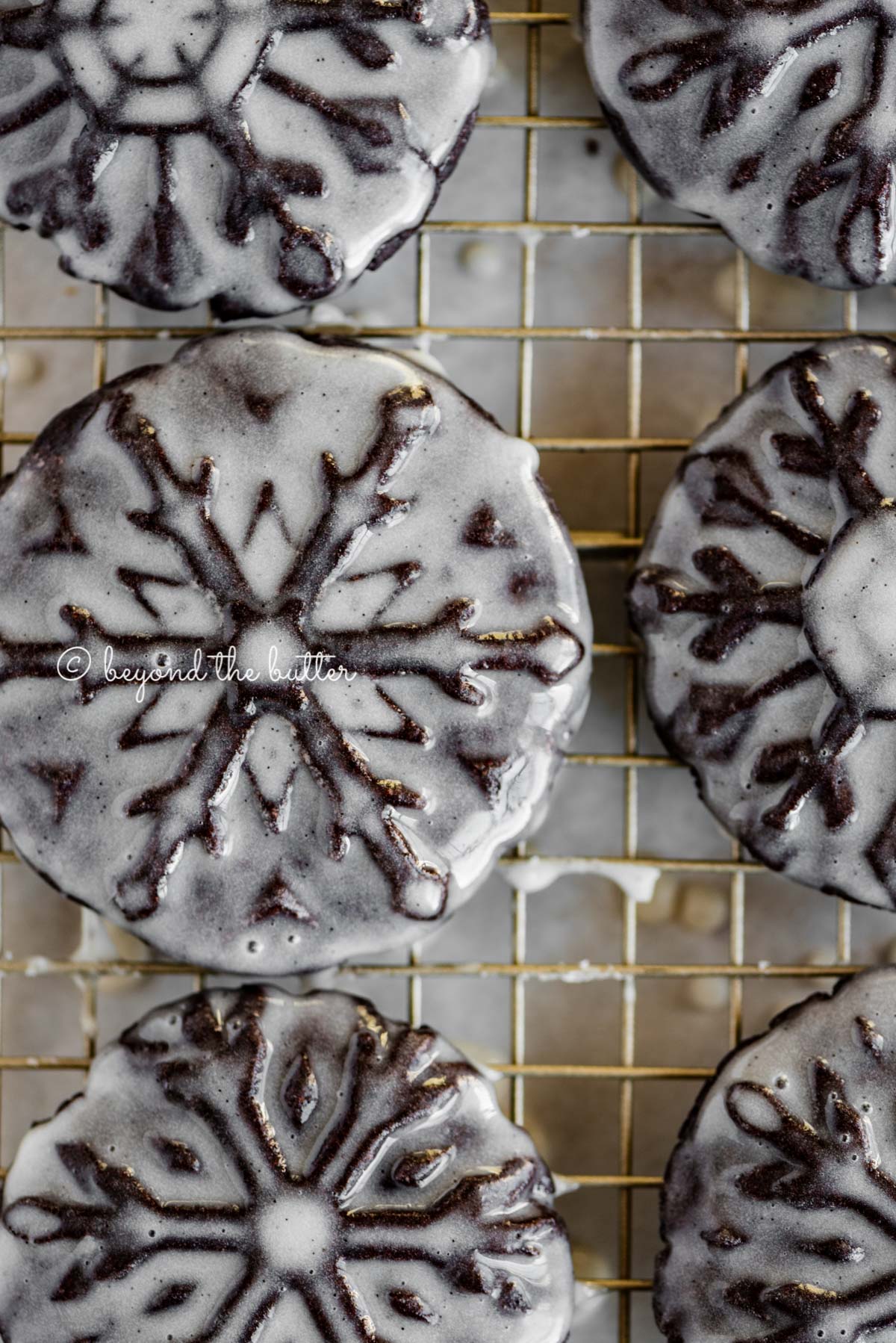Overhead closeup image of homemade oreo snowflake cookies on a wire cooling rack | All Images © Luyiz®