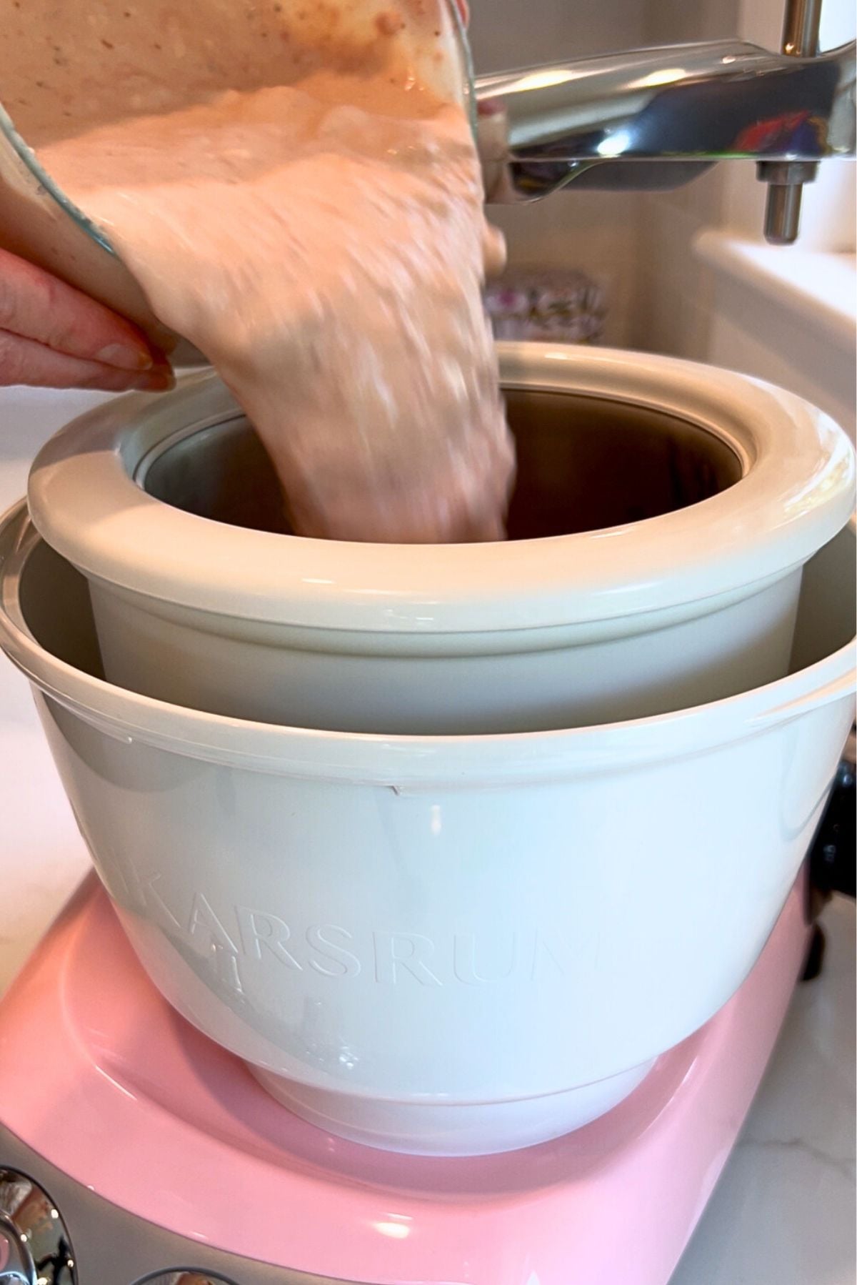 Pouring the strawberry ice cream base into the Cloudy Pink Ankarsrum Assistent Original Mixer and ice cream maker on low speed.