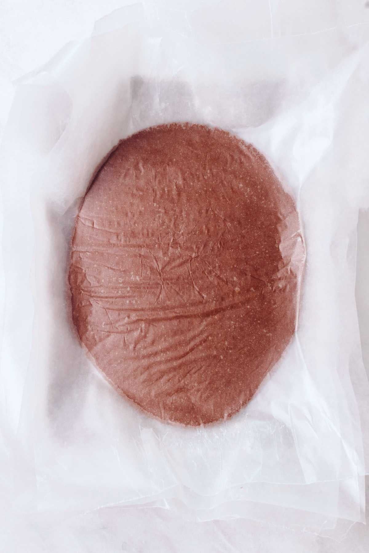 Rolled out thin mint cookie dough between two layers of wax paper on a white marbled background.