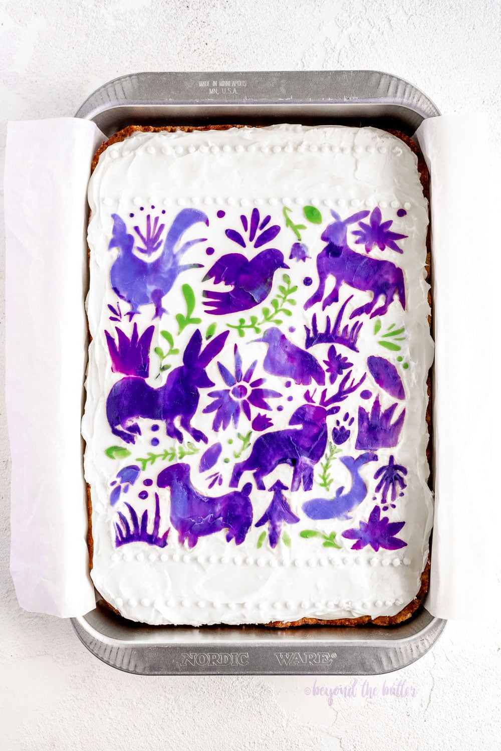 Hummingbird Sheet Cake with White Chocolate Cream Cheese Frosting | Overhead photo of Hummingbird Sheet Cake that's topped with a white chocolate frosting, and stenciled using purple and green frosting | Image and Copyright Policy: © Luyiz, LLC.