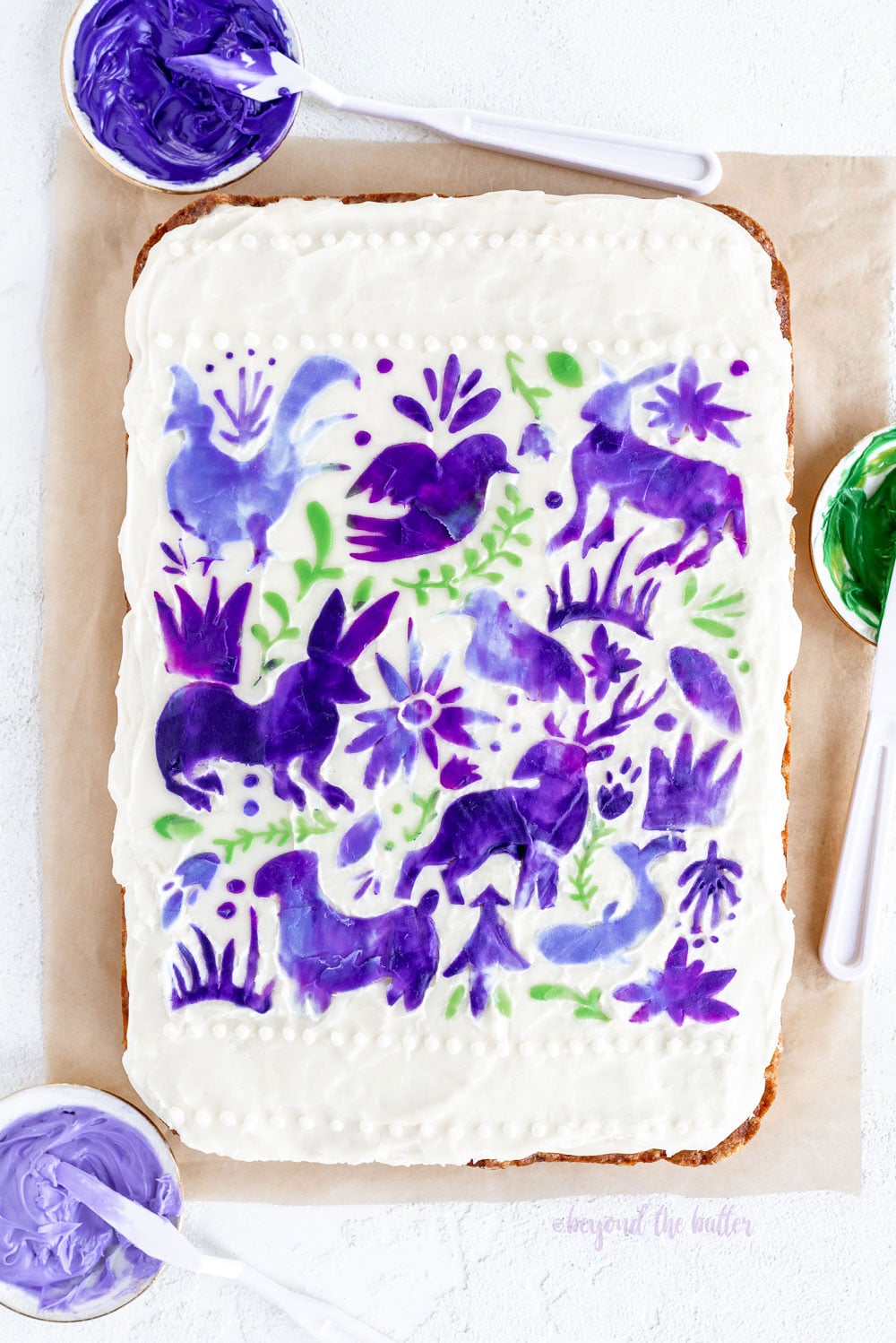 Hummingbird Sheet Cake with White Chocolate Cream Cheese Frosting | Overhead photo of Hummingbird Sheet Cake that's topped with a white chocolate frosting, and stenciled using purple and green frosting | Image and Copyright Policy: © Luyiz, LLC.