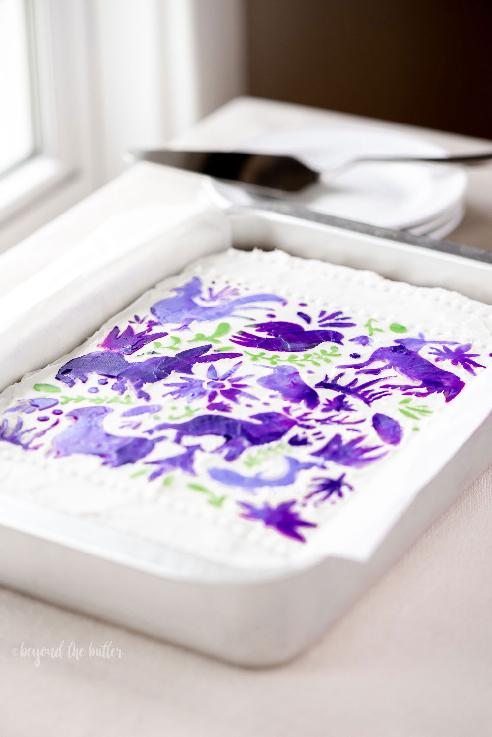 Hummingbird Sheet Cake with White Chocolate Cream Cheese Frosting | Overhead photo of Hummingbird Sheet Cake that's topped with a white chocolate frosting, and stenciled using purple and green frosting | Image and Copyright Policy: © Luyiz, LLC.