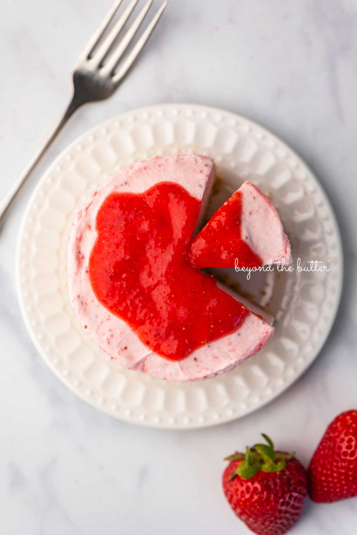 Small 4-inch no-bake strawberry cheesecake on a white dessert plate with a fork and fresh strawberries nearby on a marbled background | © Luyiz®