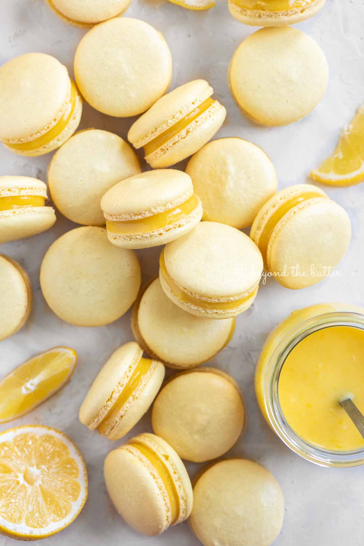 Overhead image of lemon bar macarons randomly placed around a small jar of lemon curd filling | All Images © Luyiz™