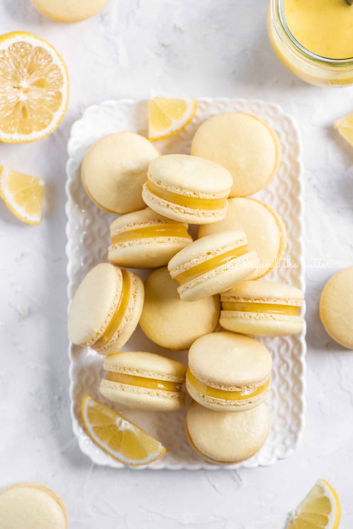 Overhead image of lemon bar macarons on a white dessert tray with lemon wedges | All Images © Luyiz™
