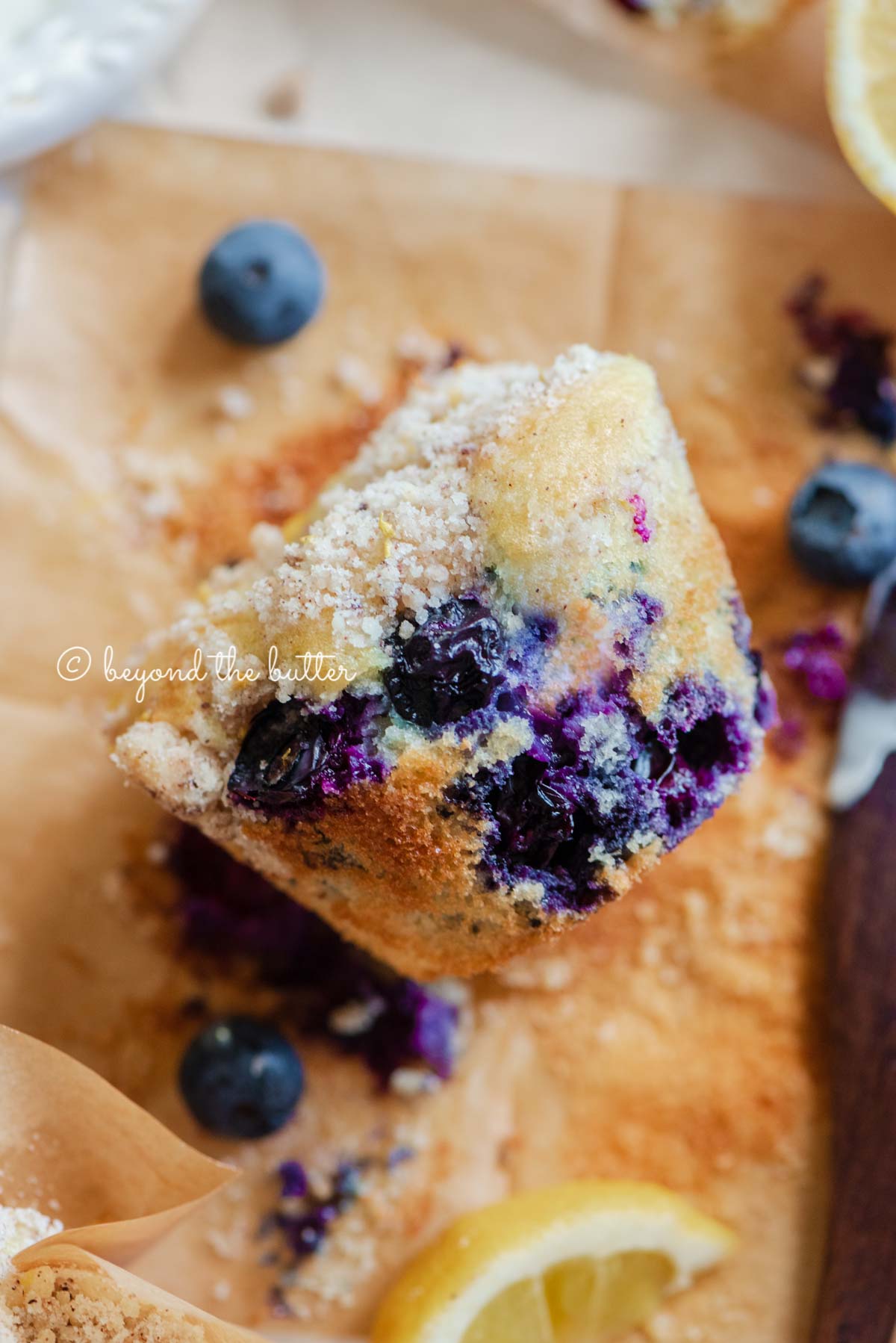 Unwrapped lemon blueberry streusel muffin with lemon wedges and blueberries around it | All images © Luyiz®