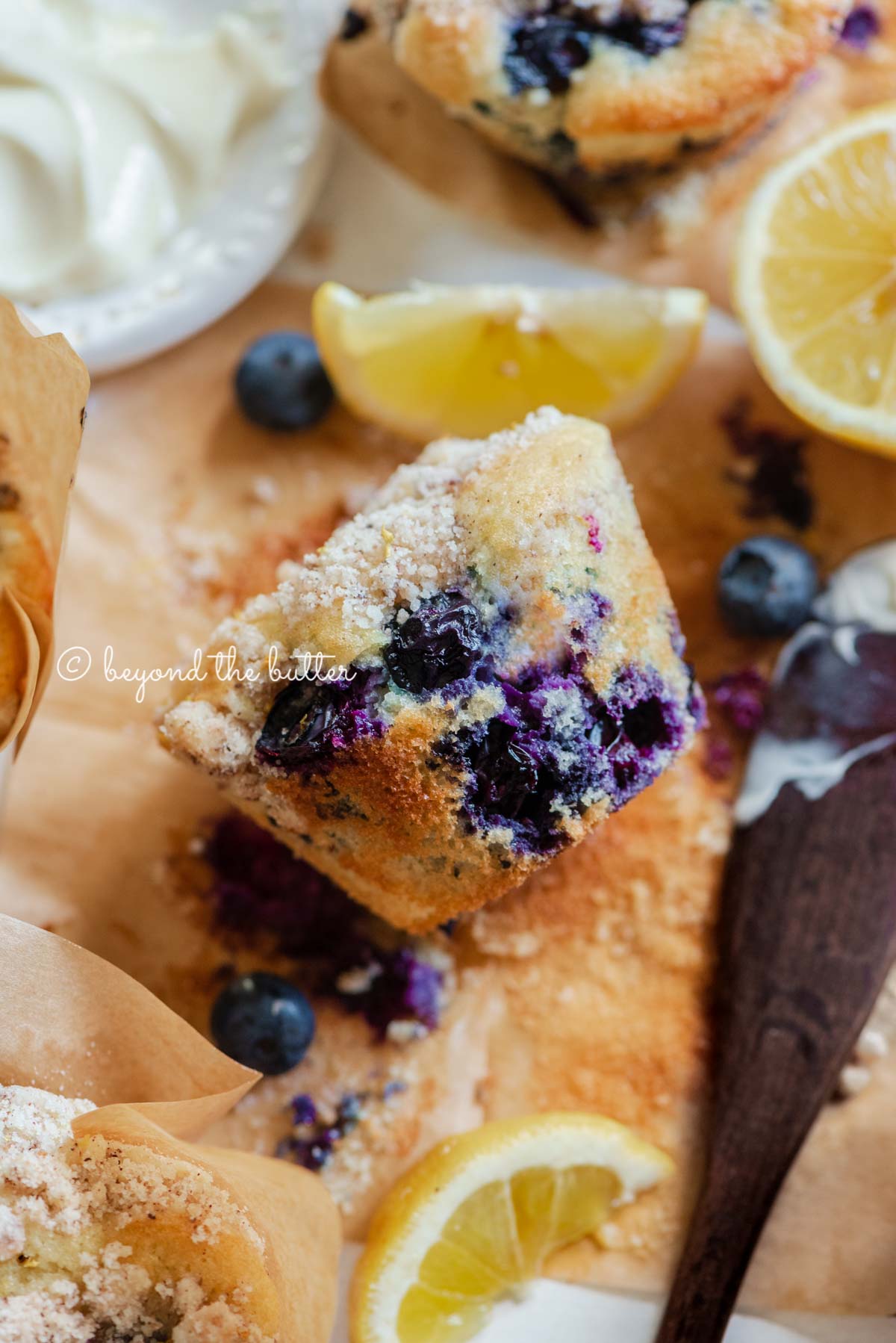 Unwrapped lemon blueberry streusel muffin with small bowl of butter, lemon wedges and blueberries around it | All images © Luyiz®