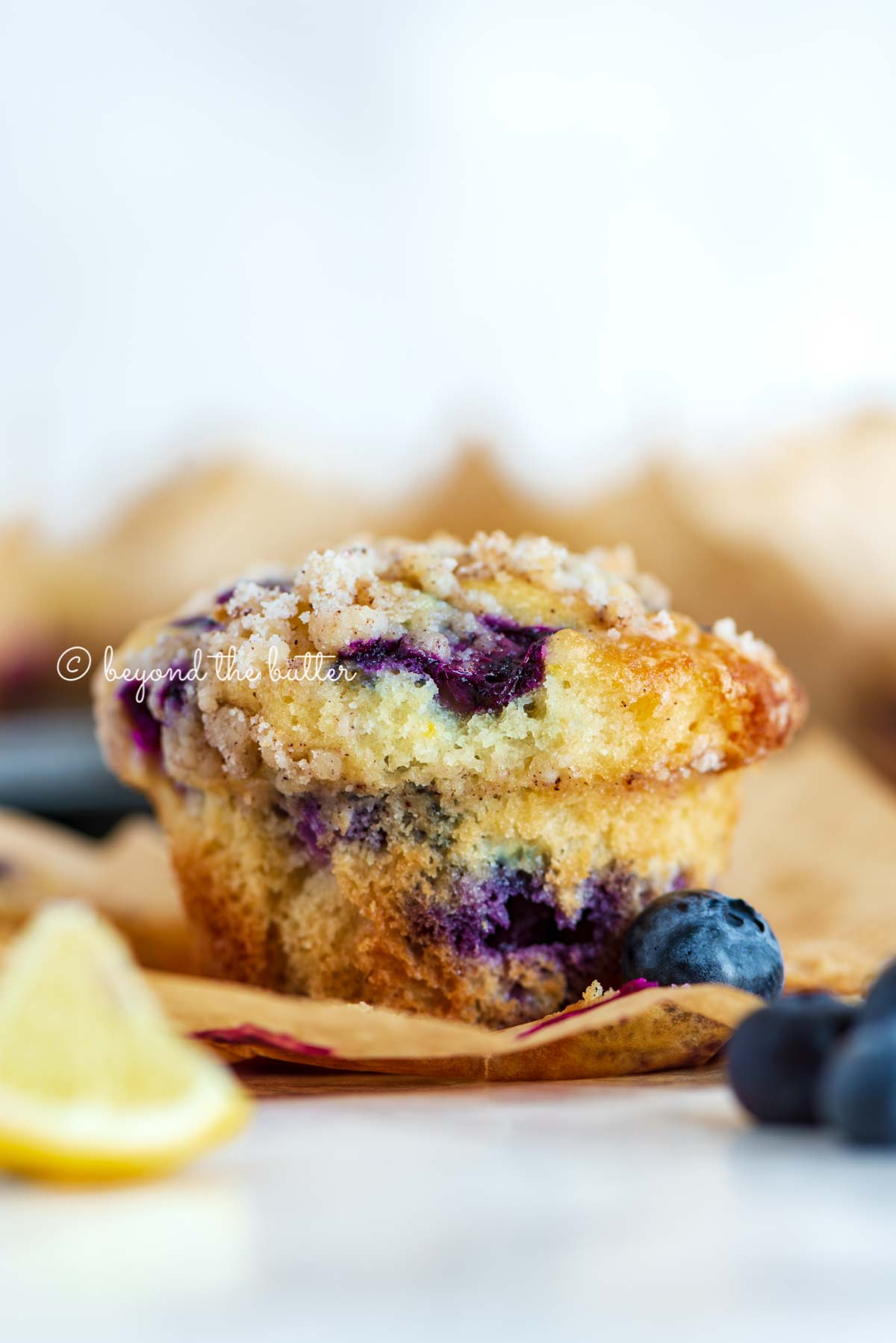 Unwrapped lemon blueberry streusel muffin with lemon wedges and blueberries around it | All images © Luyiz®