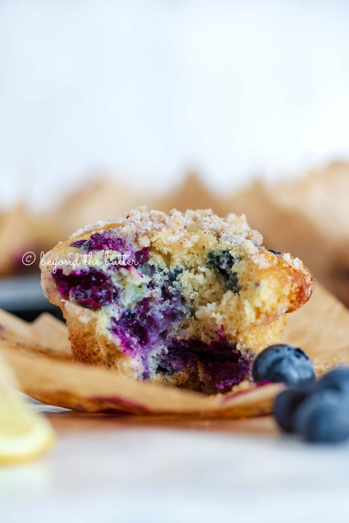 Unwrapped and half eaten lemon blueberry streusel muffin with lemon wedges and blueberries around it | All images © Luyiz®