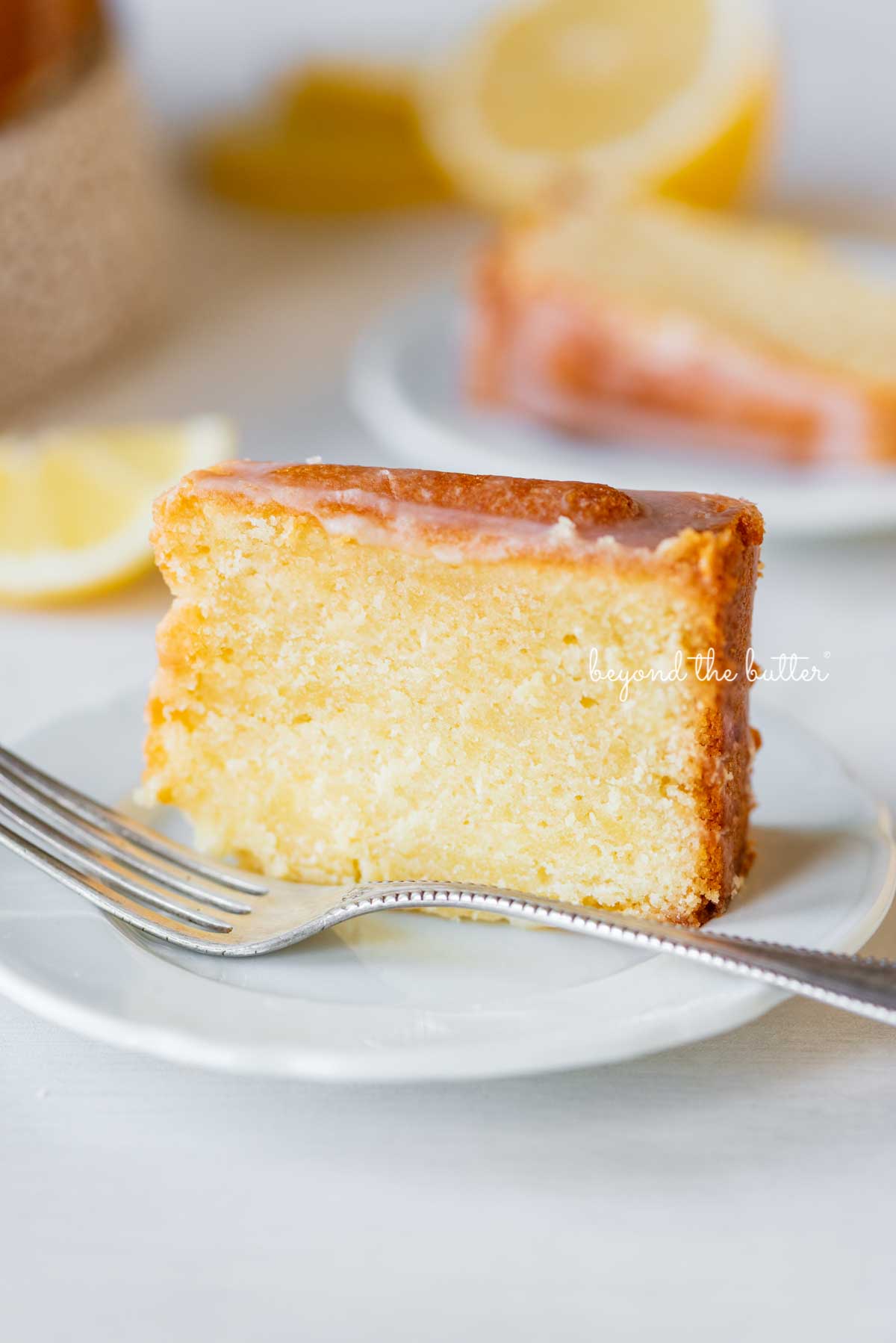 Single slice of glazed lemon cream cheese pound cake on a white dessert plate | © Luyiz®