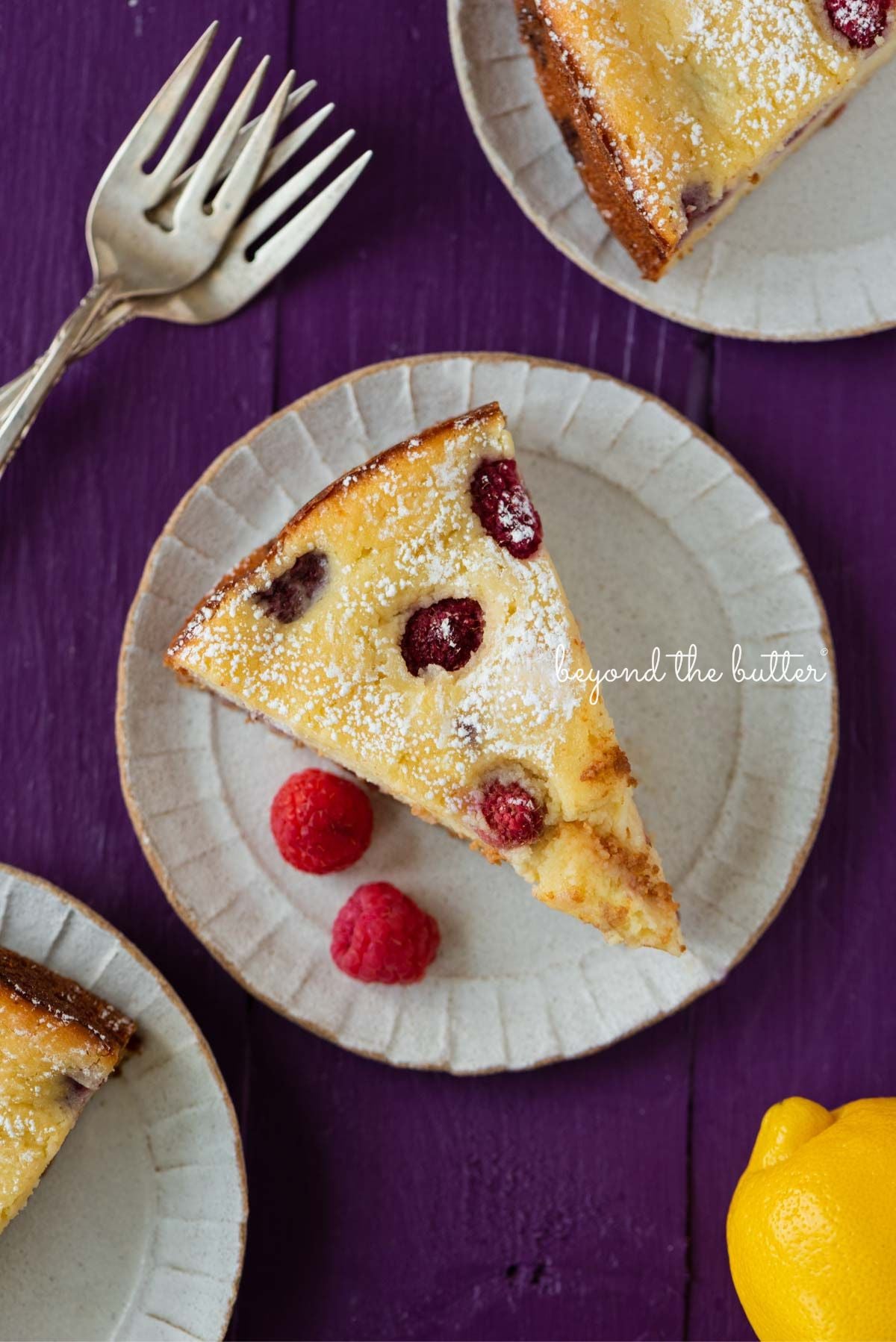 Slices of lemon raspberry ricotta cake dusted with powdered sugar on small ceramic dessert plates and purple wood background.