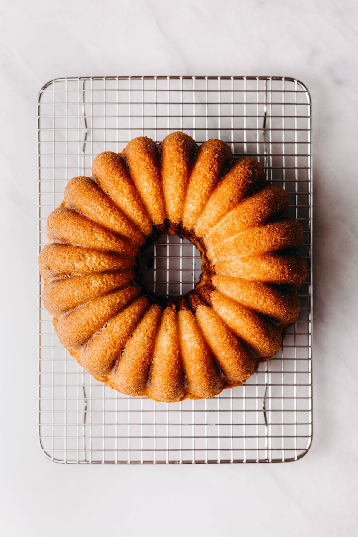 Cooling a marble bundt cake on a wire cooling rack on a white marbled background.