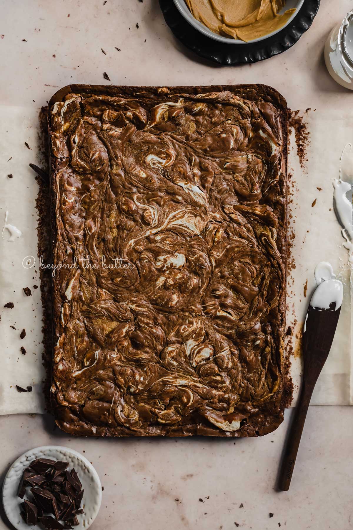 Uncut marshmallow peanut butter brownies on parchment paper and bowl of marshmallow fluff and spreader tool beside it | All Images © Luyiz™