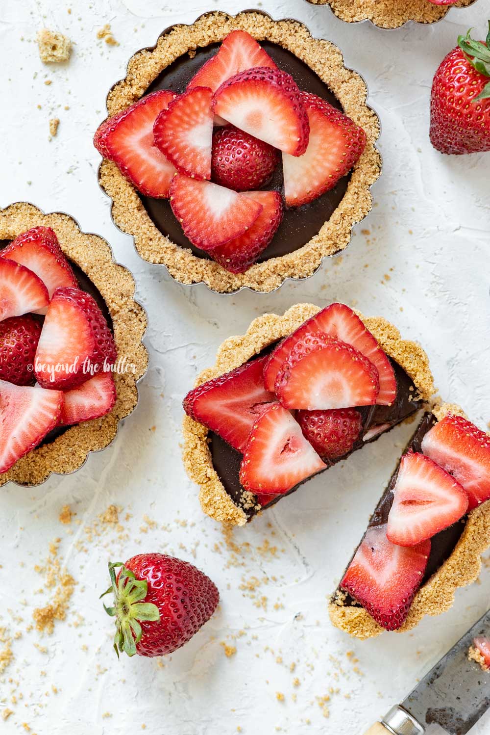 Overhead image of mini strawberry nutella tarts on white stucco background with one sliced in half and opened | All Images © Luyiz™