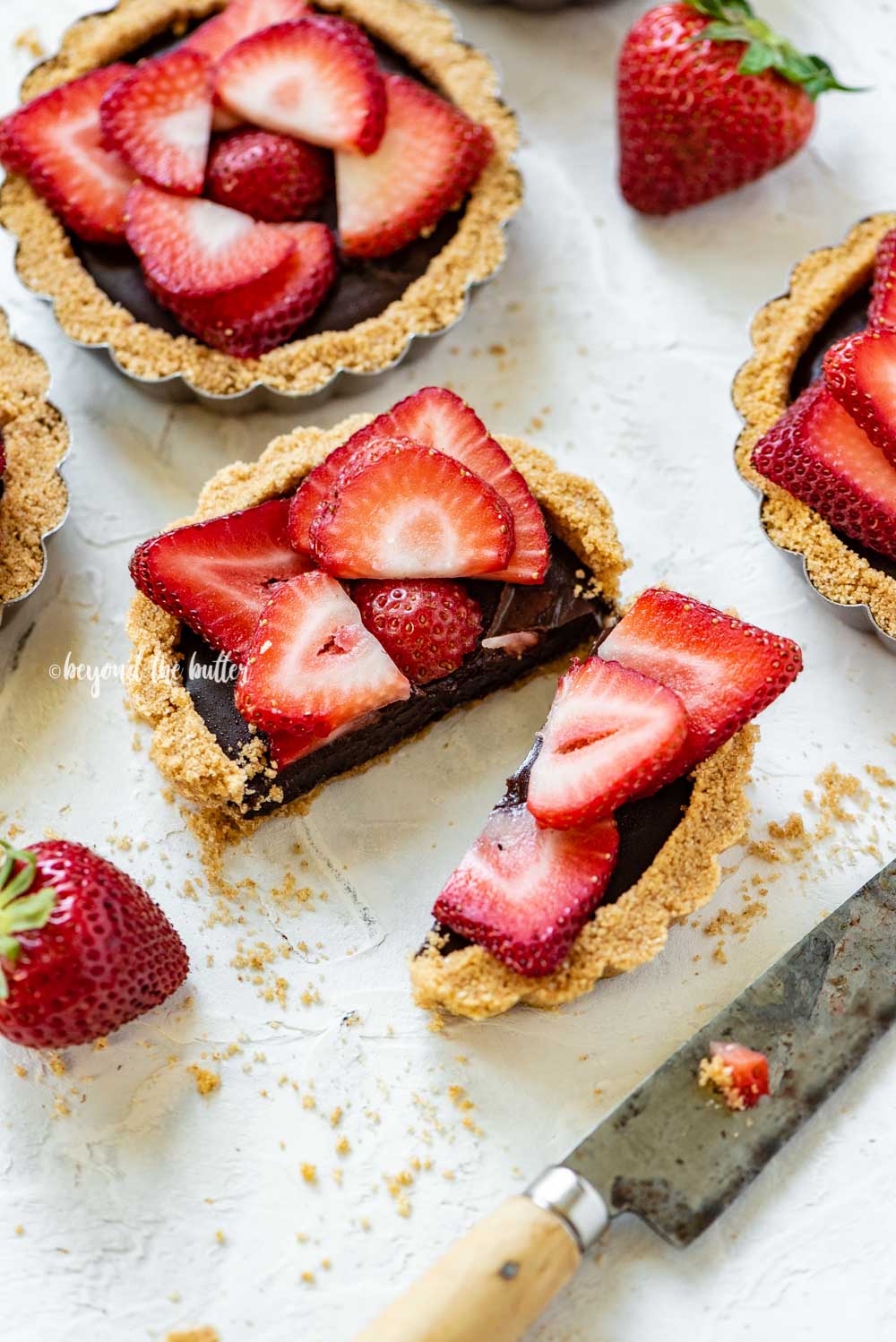 Angled image of mini strawberry nutella tarts on white stucco background with one sliced in half and opened | All Images © Luyiz™