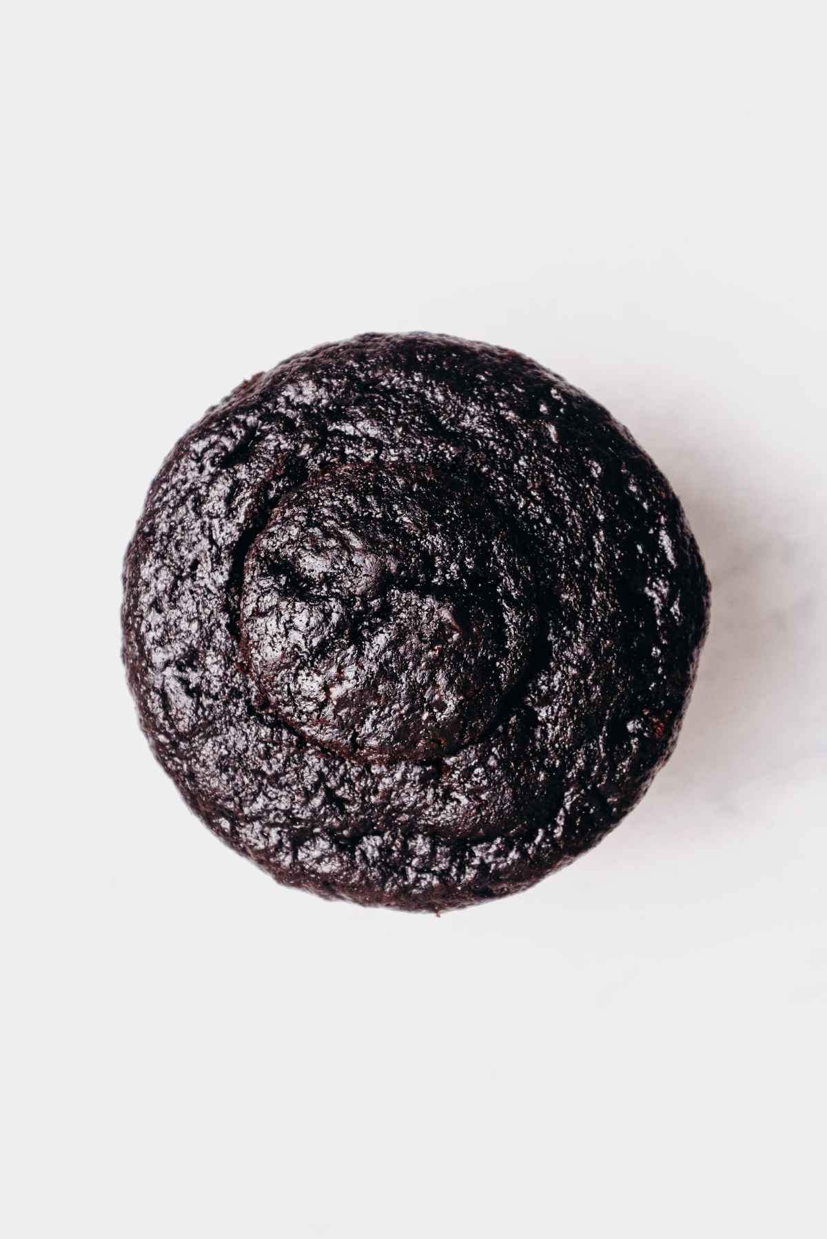 One chocolate cupcake filled with mint chocolate ganache topped with round piece of chocolate cupcake on a grey marbled background.