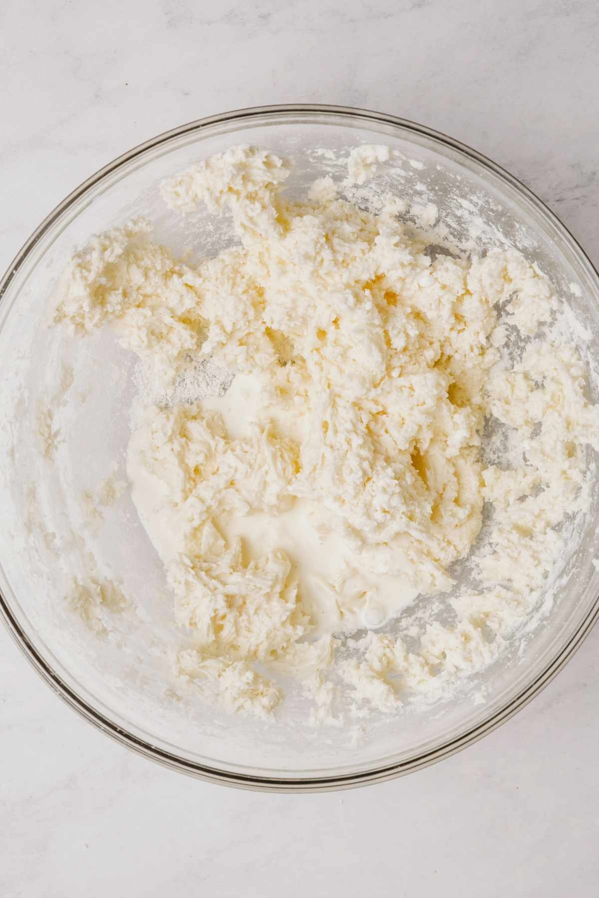 Powdered sugar and peppermint extract whisked together with unsalted butter in large glass mixing bowl on a grey marbled background.