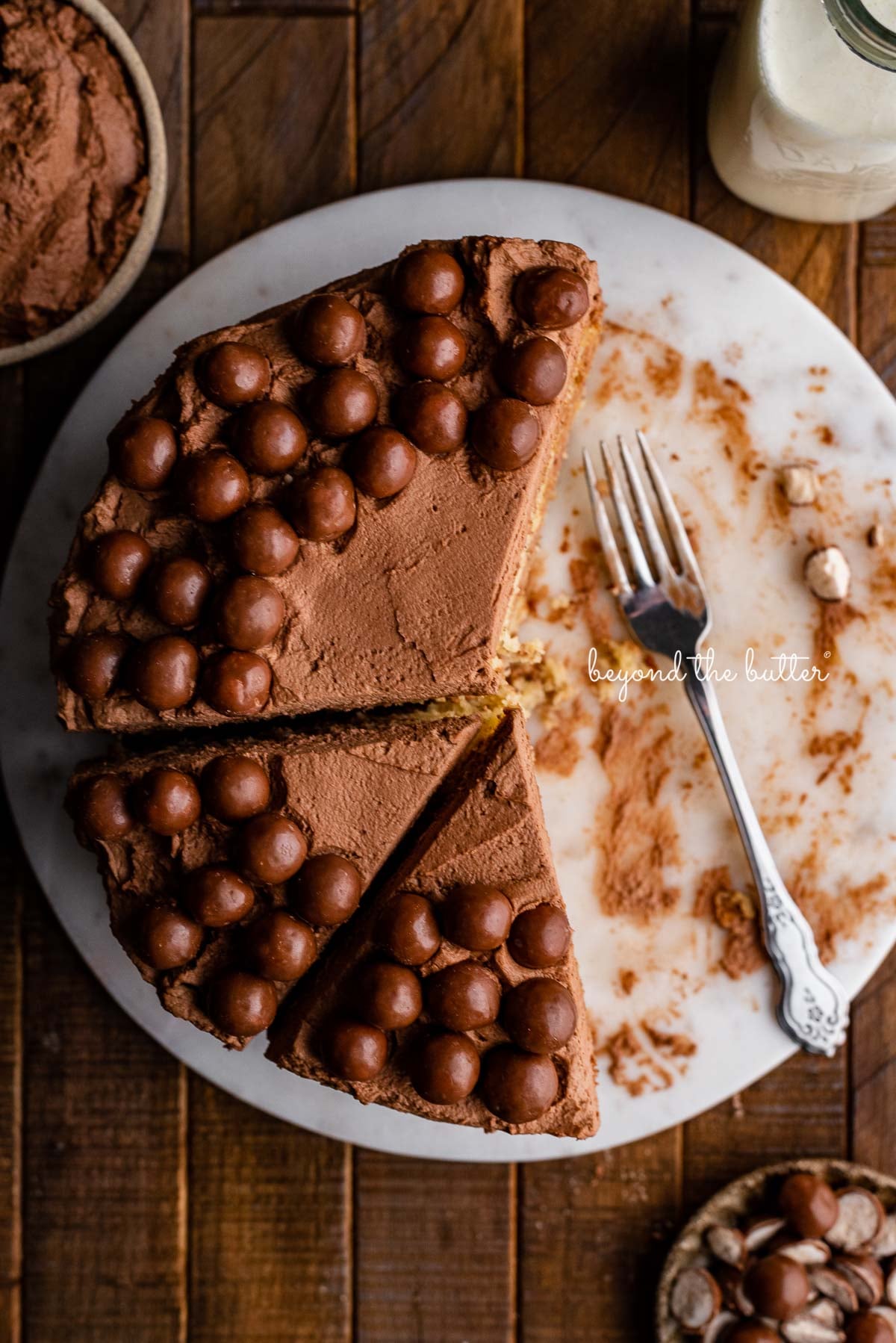 Top down view of 2 layer moist banana cake frosted with malted chocolate mascarpone whipped cream and garnished with malted chocolate balls on marble cake board | © Luyiz®