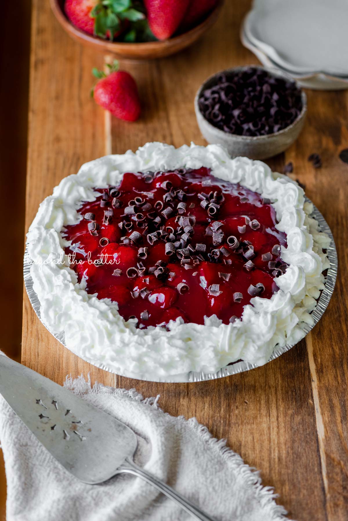 Decorated no bake strawberry chocolate pie with small bowl of chocolate curls and strawberries, dessert plates, and pie server on wood table | All images © Luyiz®