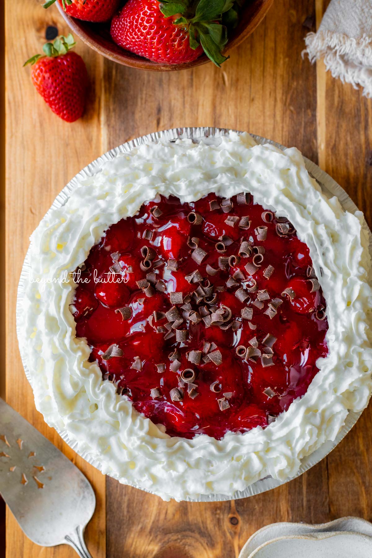 Decorated no bake strawberry chocolate pie with small bowl of strawberries, dessert plates, and pie server on wood table | All images © Luyiz®