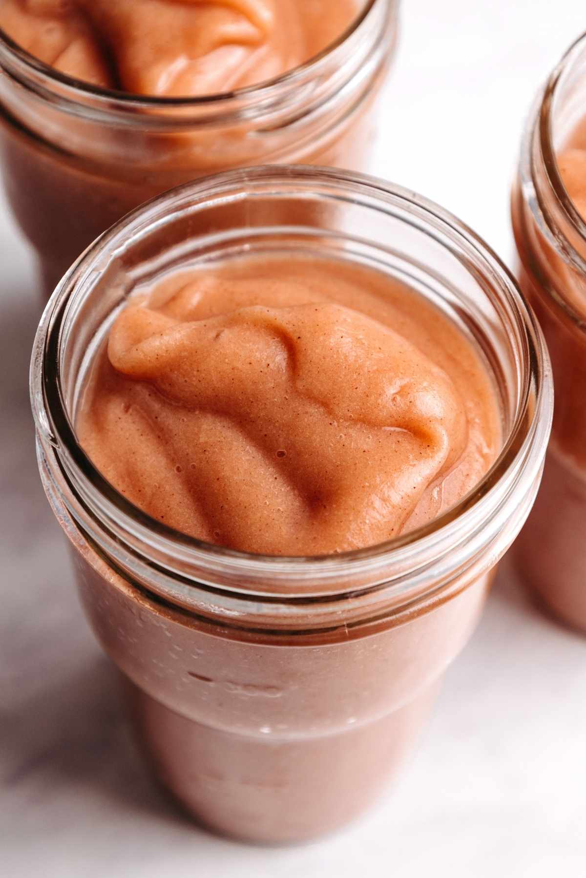 Homemade cinnamon applesauce in glass ball jars on a white background.