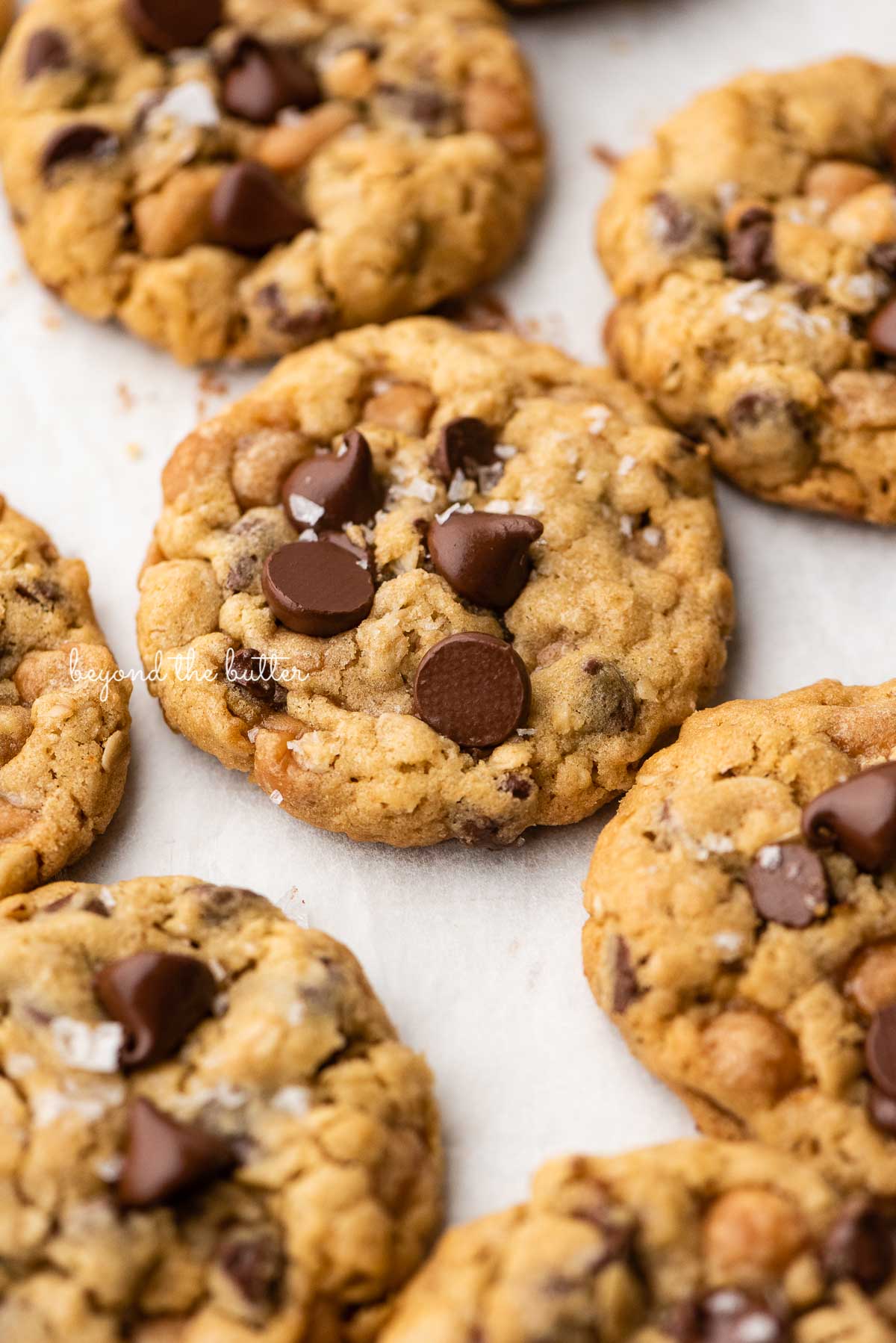 Oatmeal chocolate chip salted caramel cookies topped with flaky sea salt on a parchment paper lined baking sheet | © Luyiz®