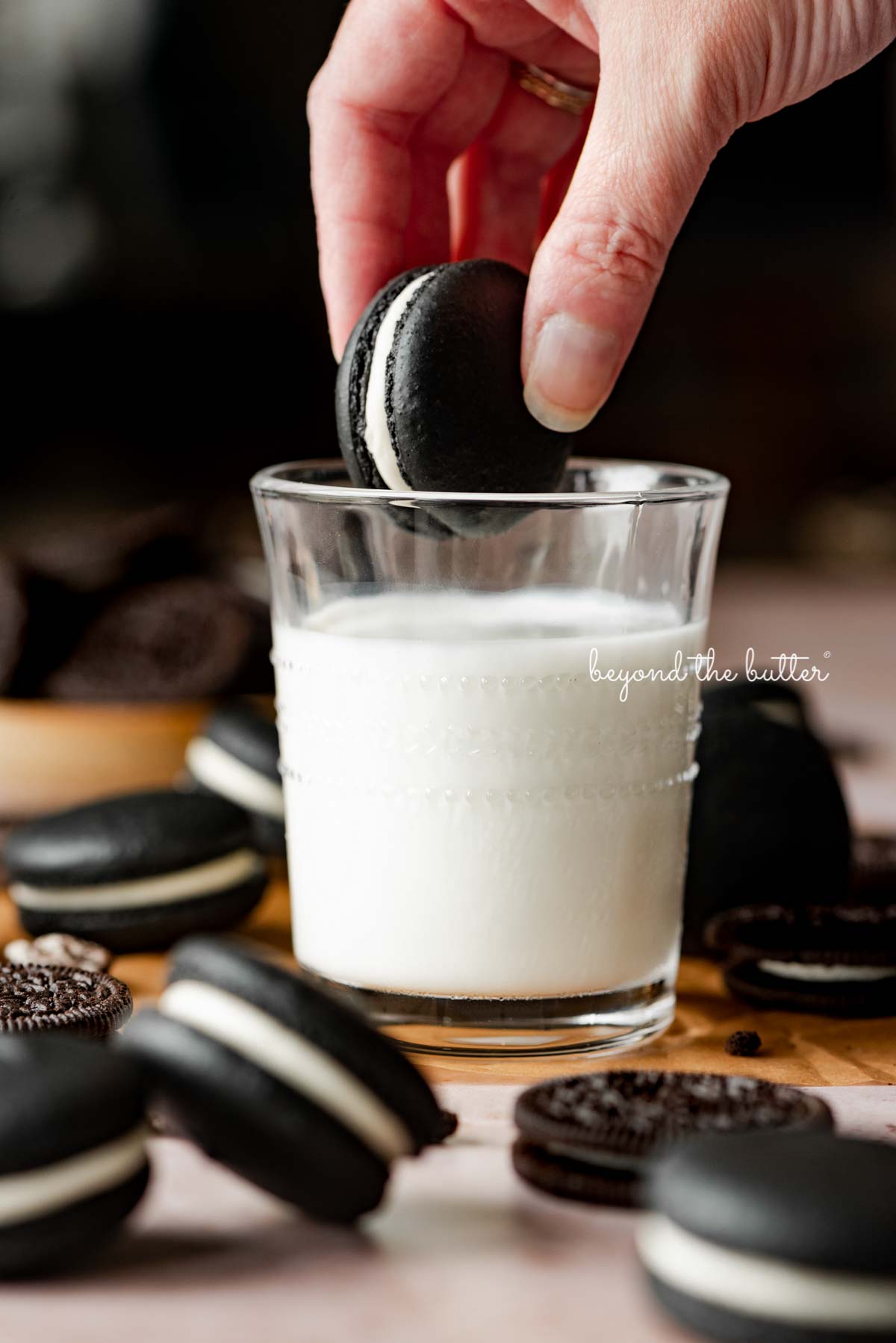 Hand dipping an oreo macaron in a glass of milk with more oreo macarons and oreo cookies around it | © Luyiz®