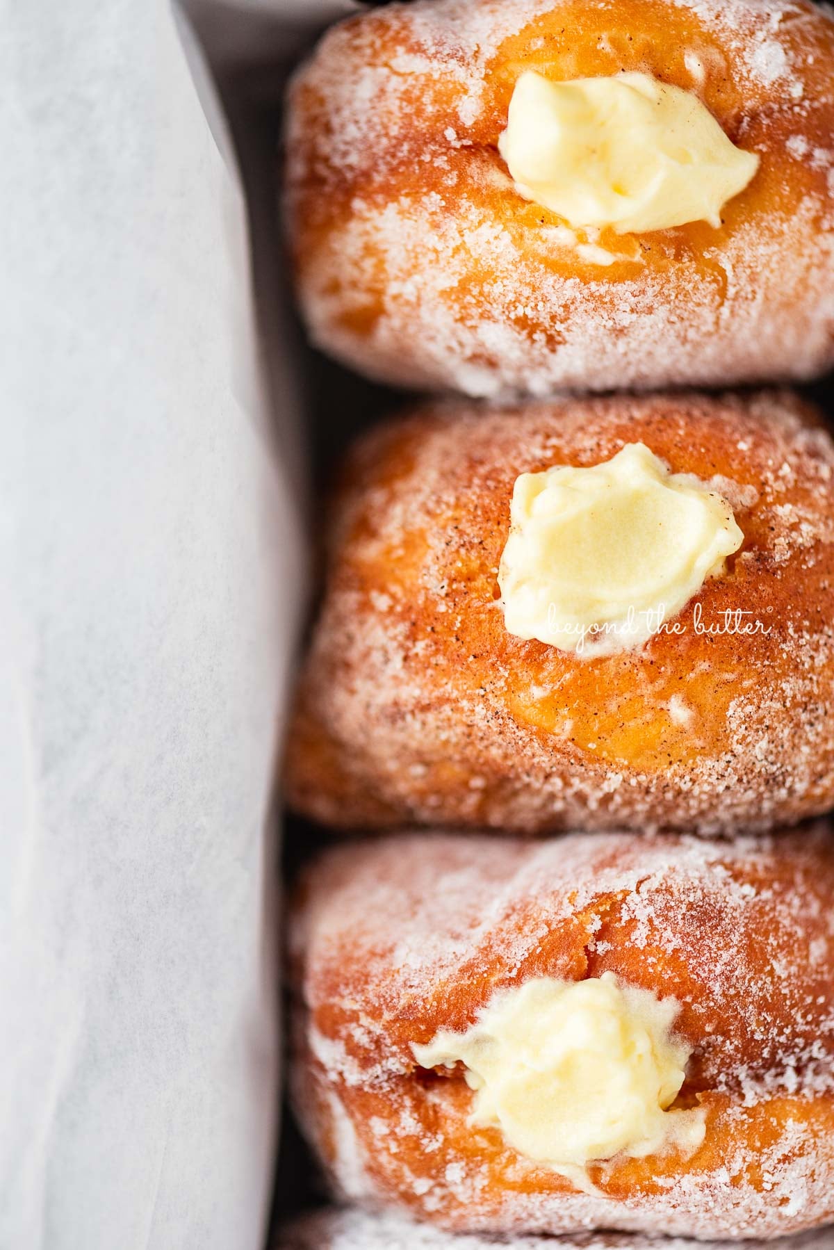 Close up of homemade pennsylvania dutch fasnacht doughnuts filled with vanilla pastry cream wrapped in parchment paper in a loaf pan | © Luyiz®