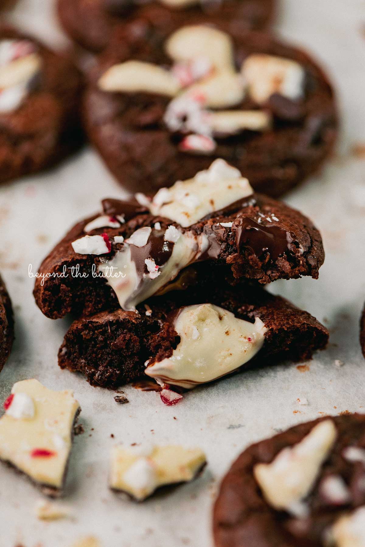 A split peppermint bark brownie crinkle cookie on a parchment paper lined baking sheet | © Beyond the Buter®