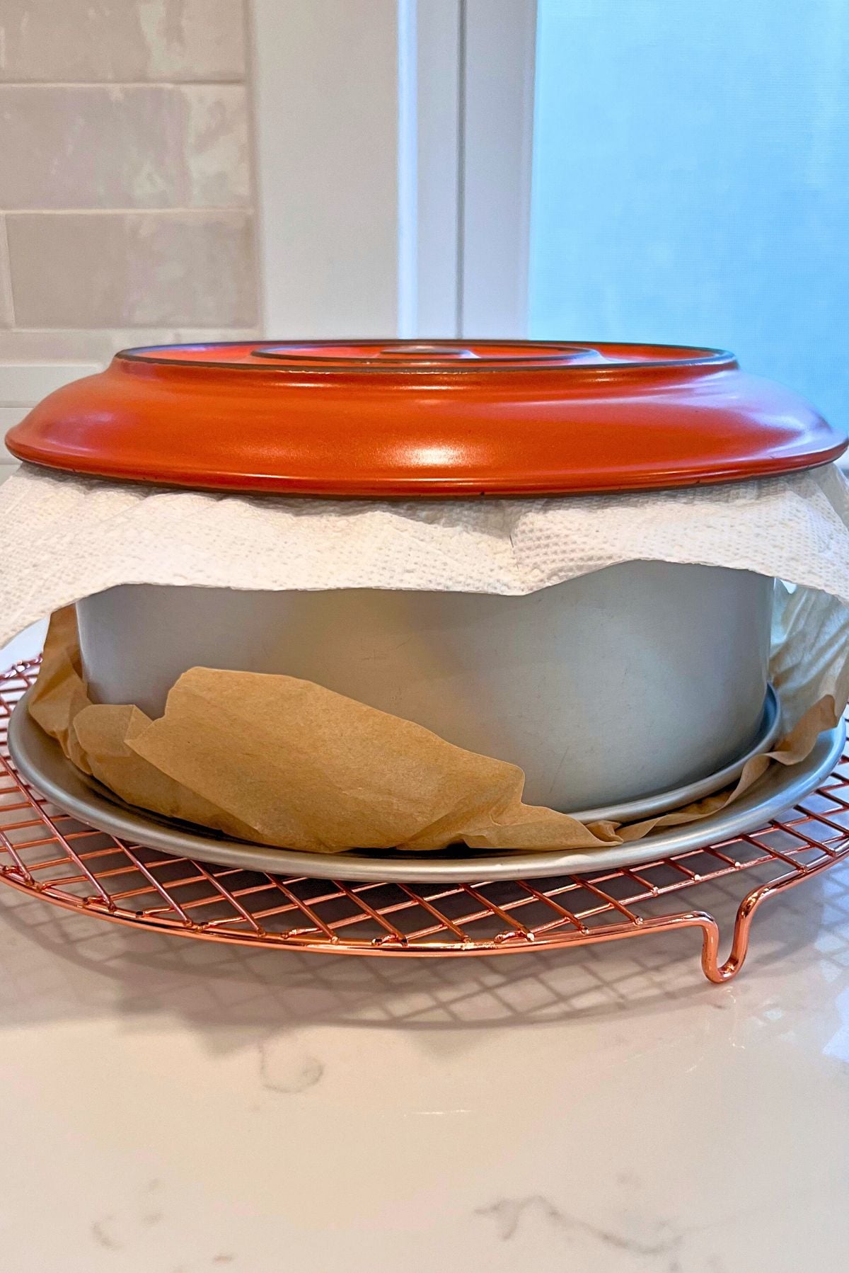 Pumpkin cheesecake on a round wire cooling rack covered with a paper towel and an orange dinner plate placed upside down.