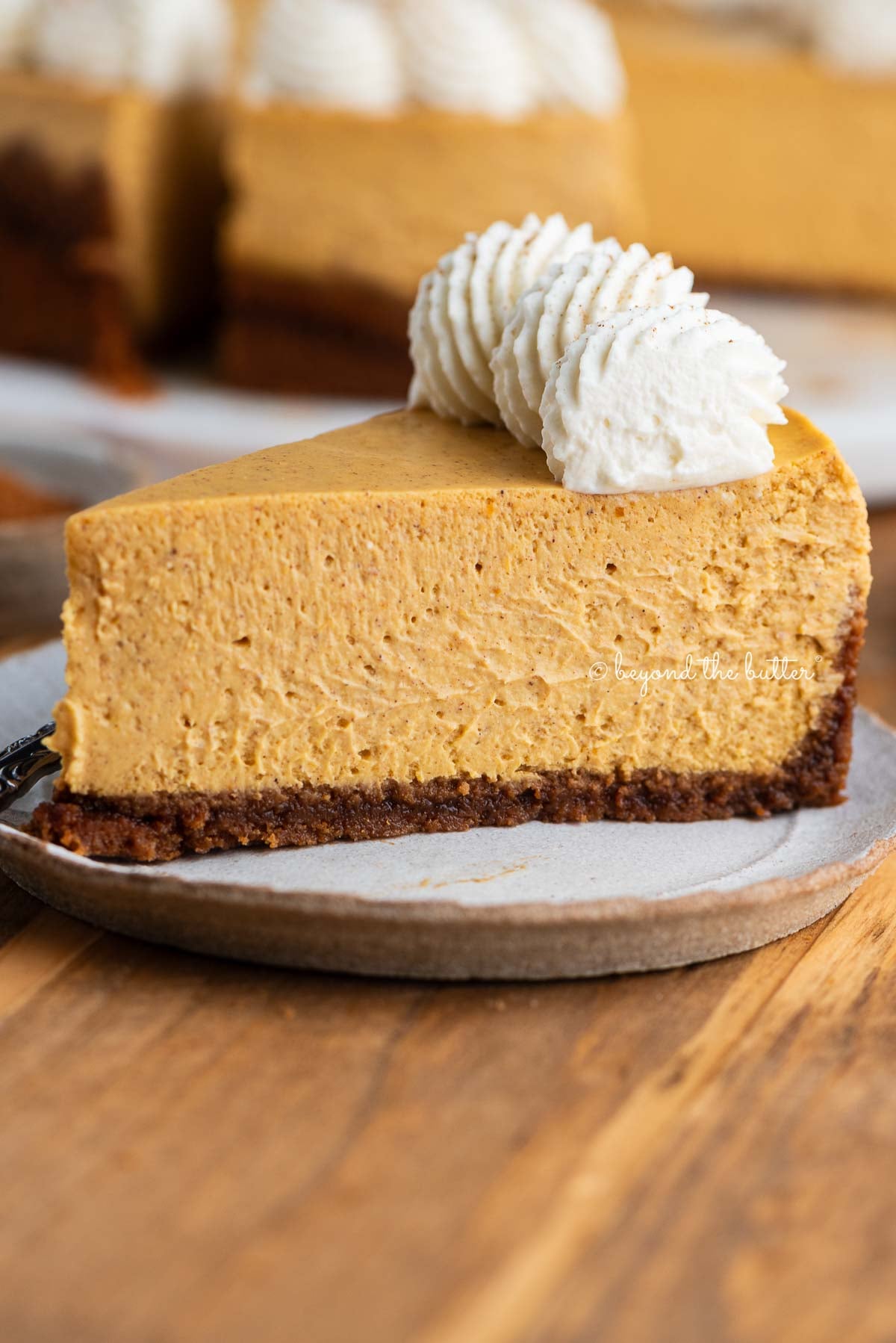 Slice of pumpkin cheesecake on a ceramic dessert plate and wood background.