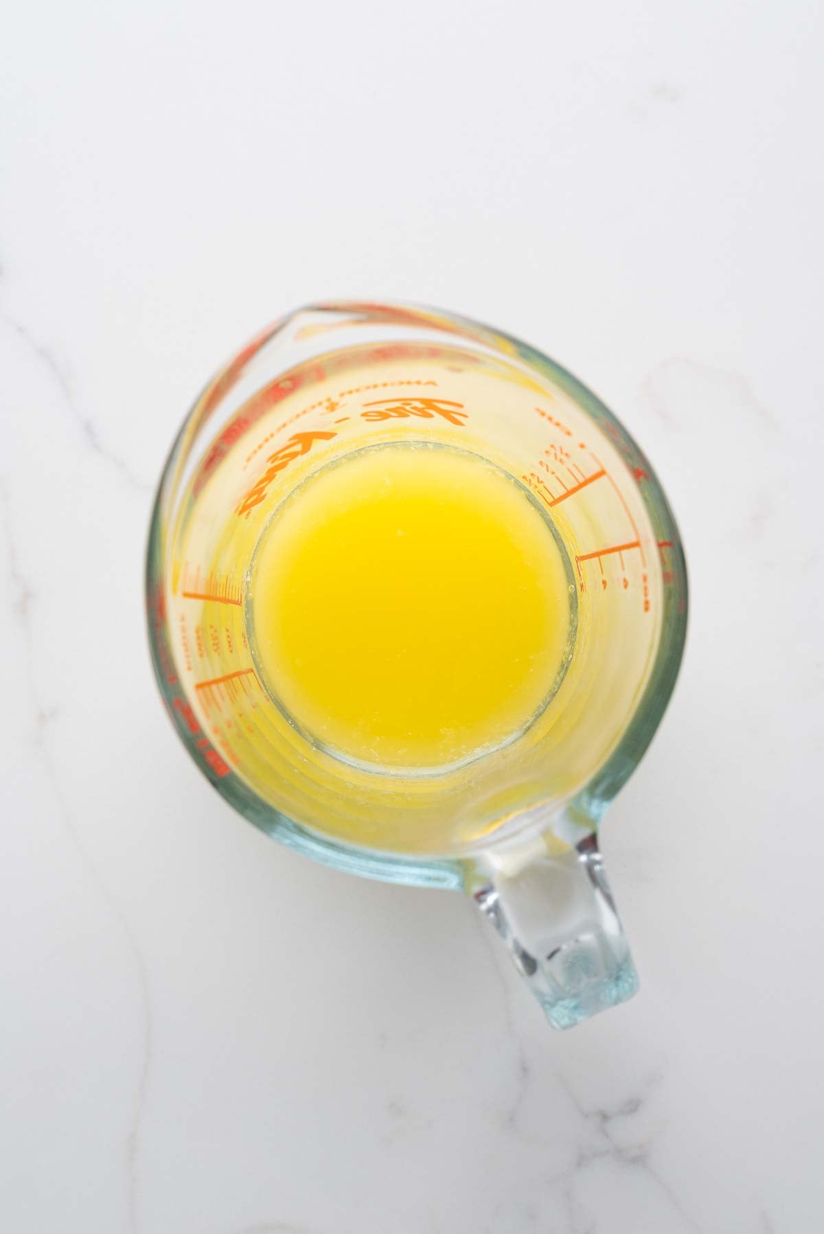 Melted unsalted butter in a glass measuring cup on a white marbled background.