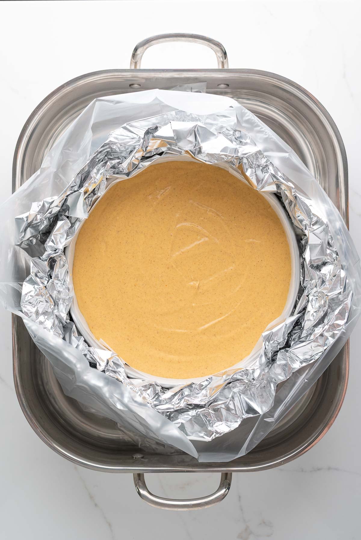 Baking a pumpkin cheesecake in a roasting pan water bath filled with hot water.