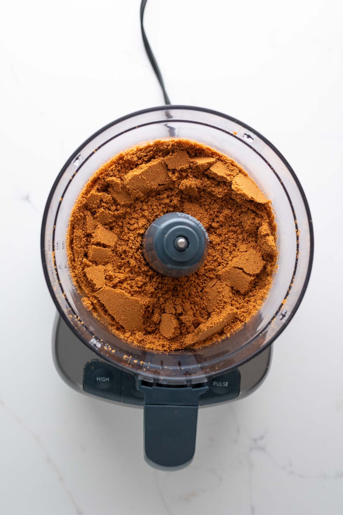 Fine speculoos cookie crumbs processed in a food processor on a white marbled background.